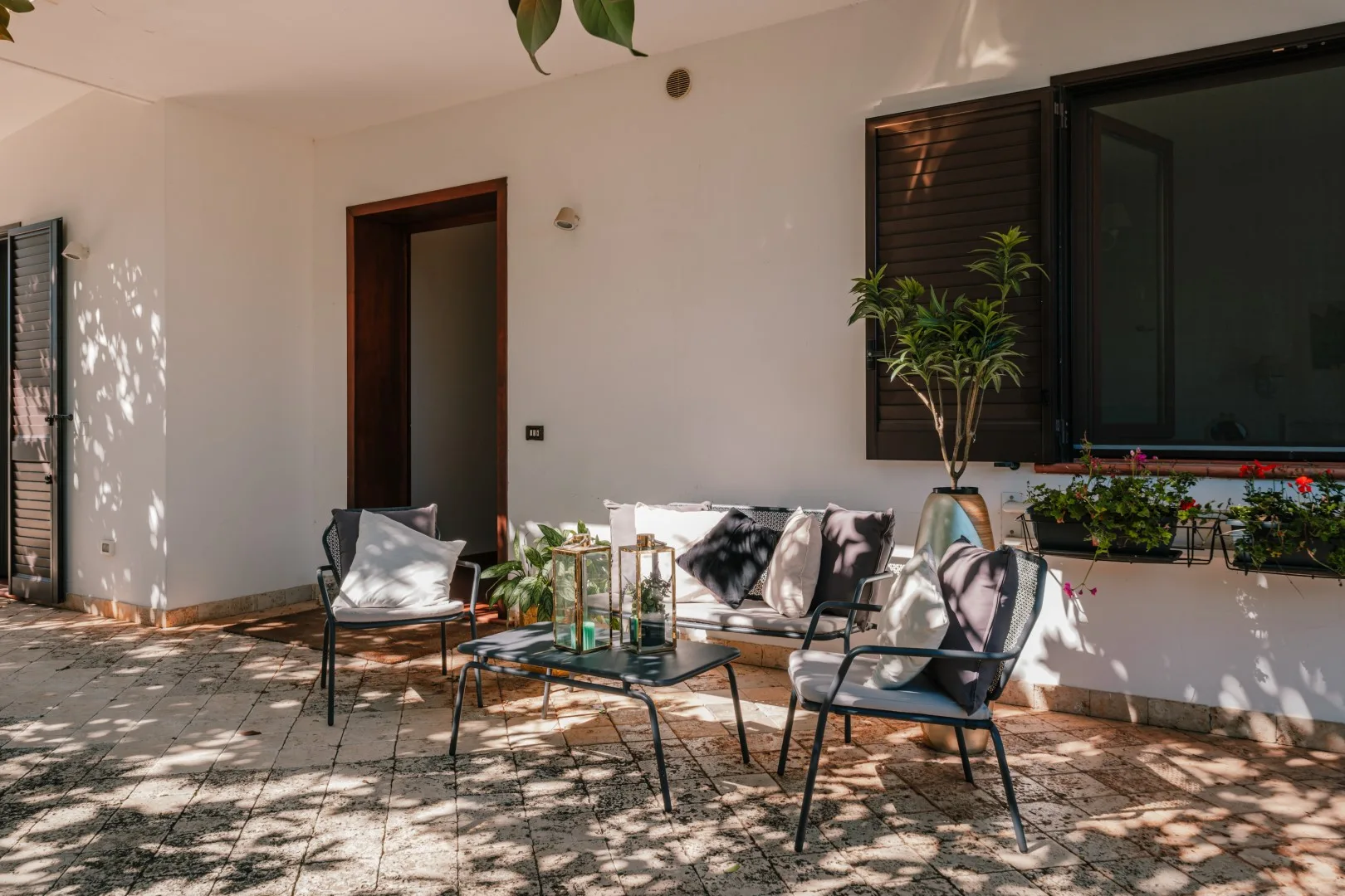 An outdoor seating area sits beside a doorway and a window with plants.