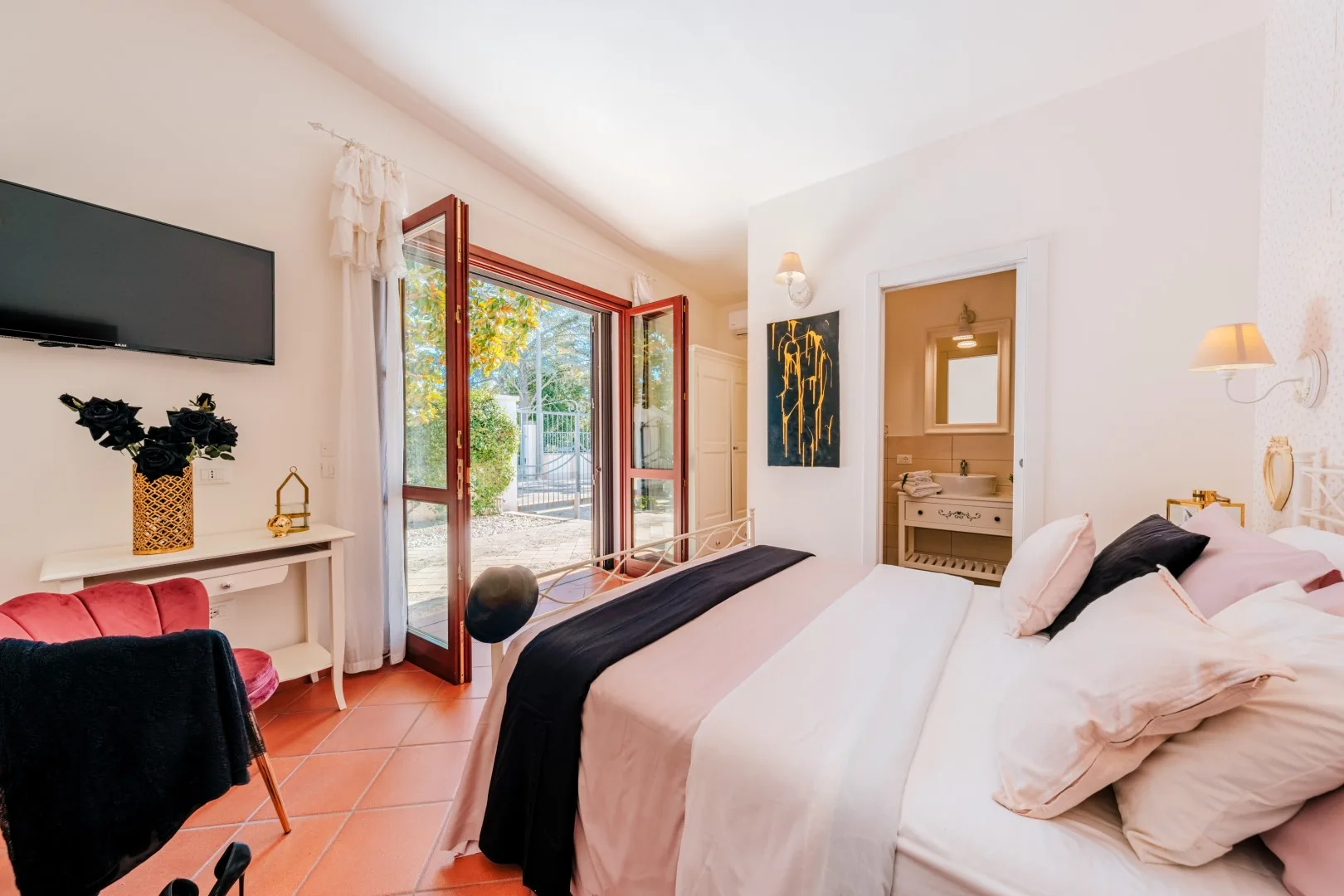 A bright bedroom with a large bed and open glass doors leading to a patio.