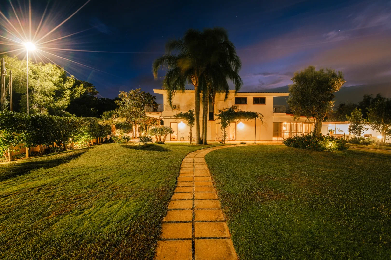 A lit building stands beyond a curved path across a landscaped lawn at dusk.