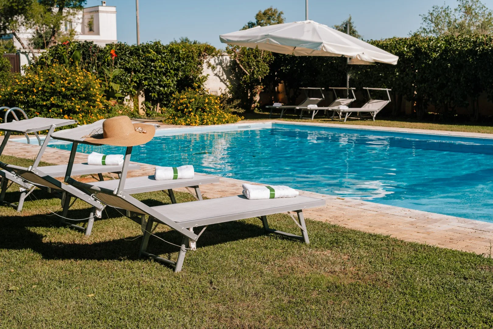 An outdoor swimming pool is bordered by sun loungers and a large shade umbrella.