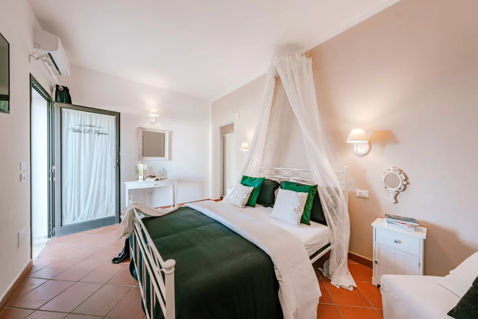 A bedroom with a canopy bed dressed in white linens and dark green bedding.