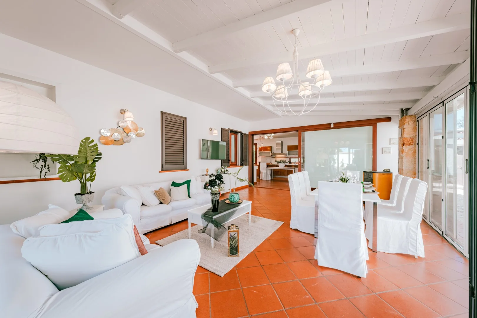 A bright living and dining area with white seating and a table beside large windows.