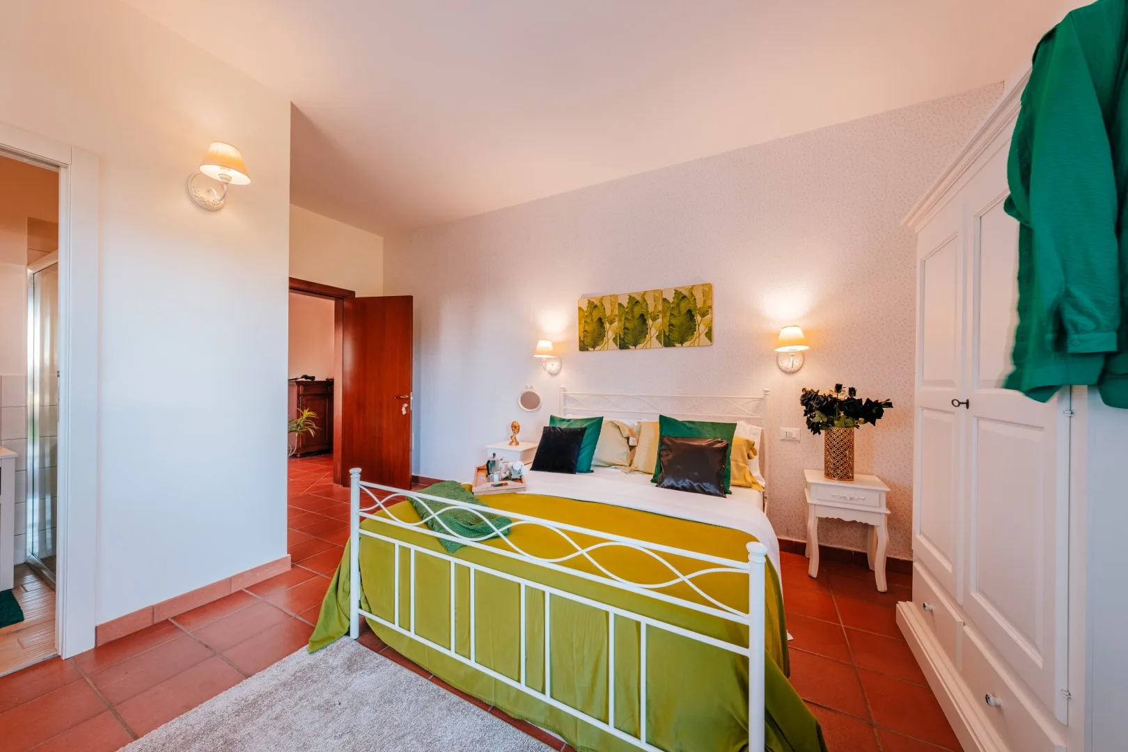 A bedroom with a metal bed, green bedding, and a small bedside table.