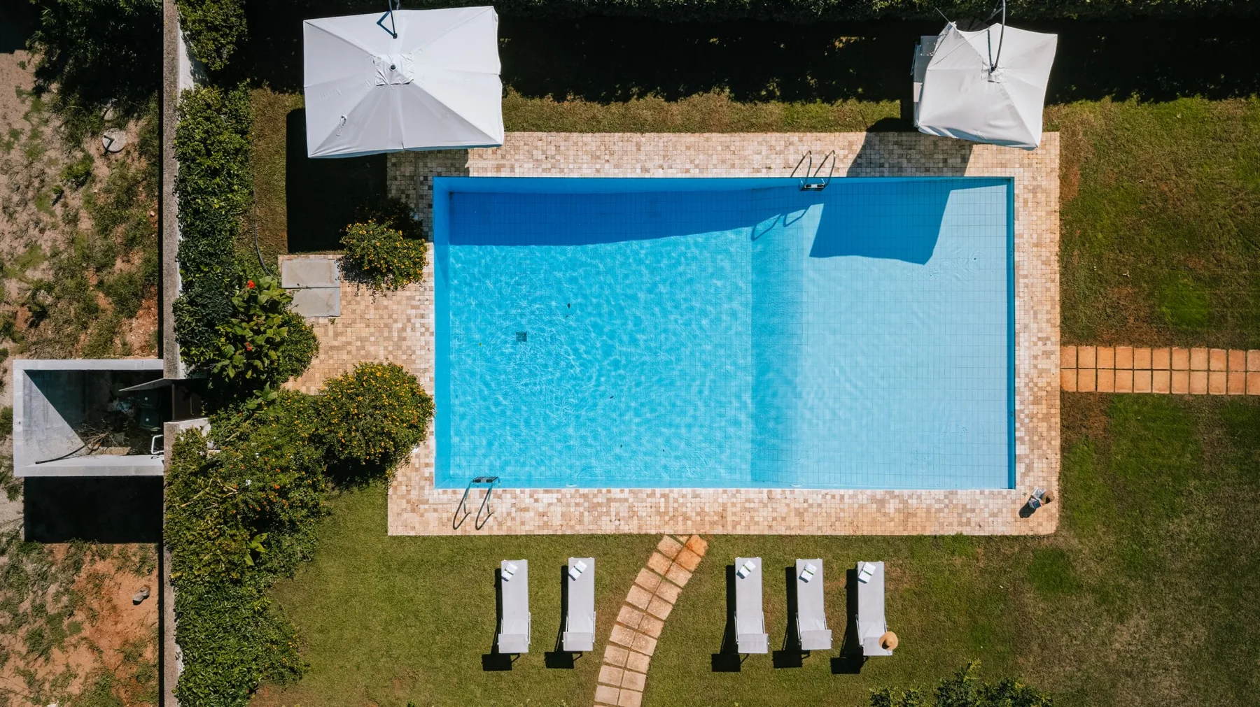 An aerial view of a rectangular swimming pool surrounded by a paved deck and lawn.