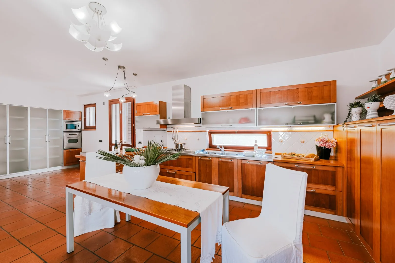 A bright kitchen with wooden cabinets, a tiled floor, and a dining table.