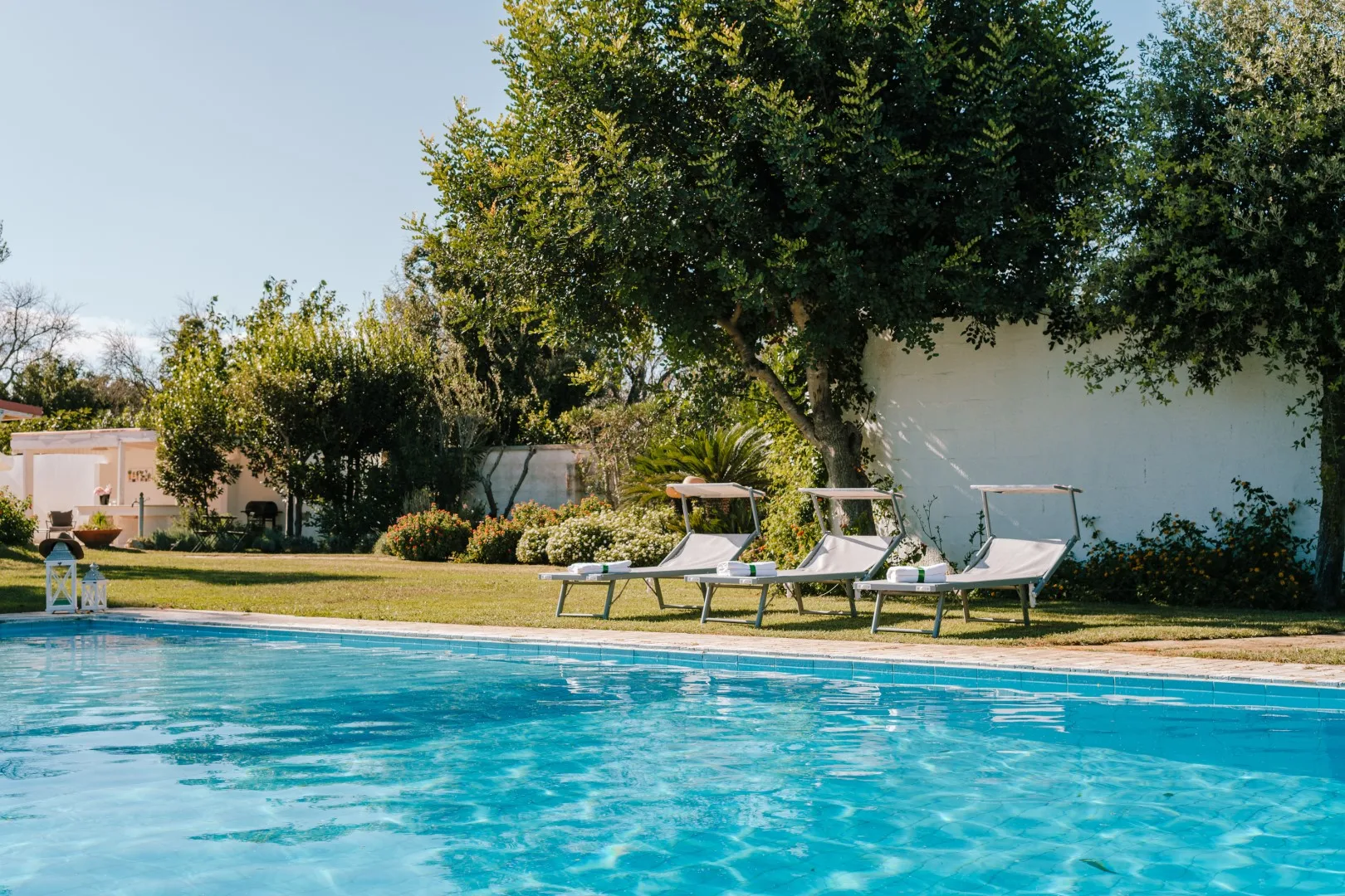 An outdoor swimming pool bordered by lounge seating and leafy trees.