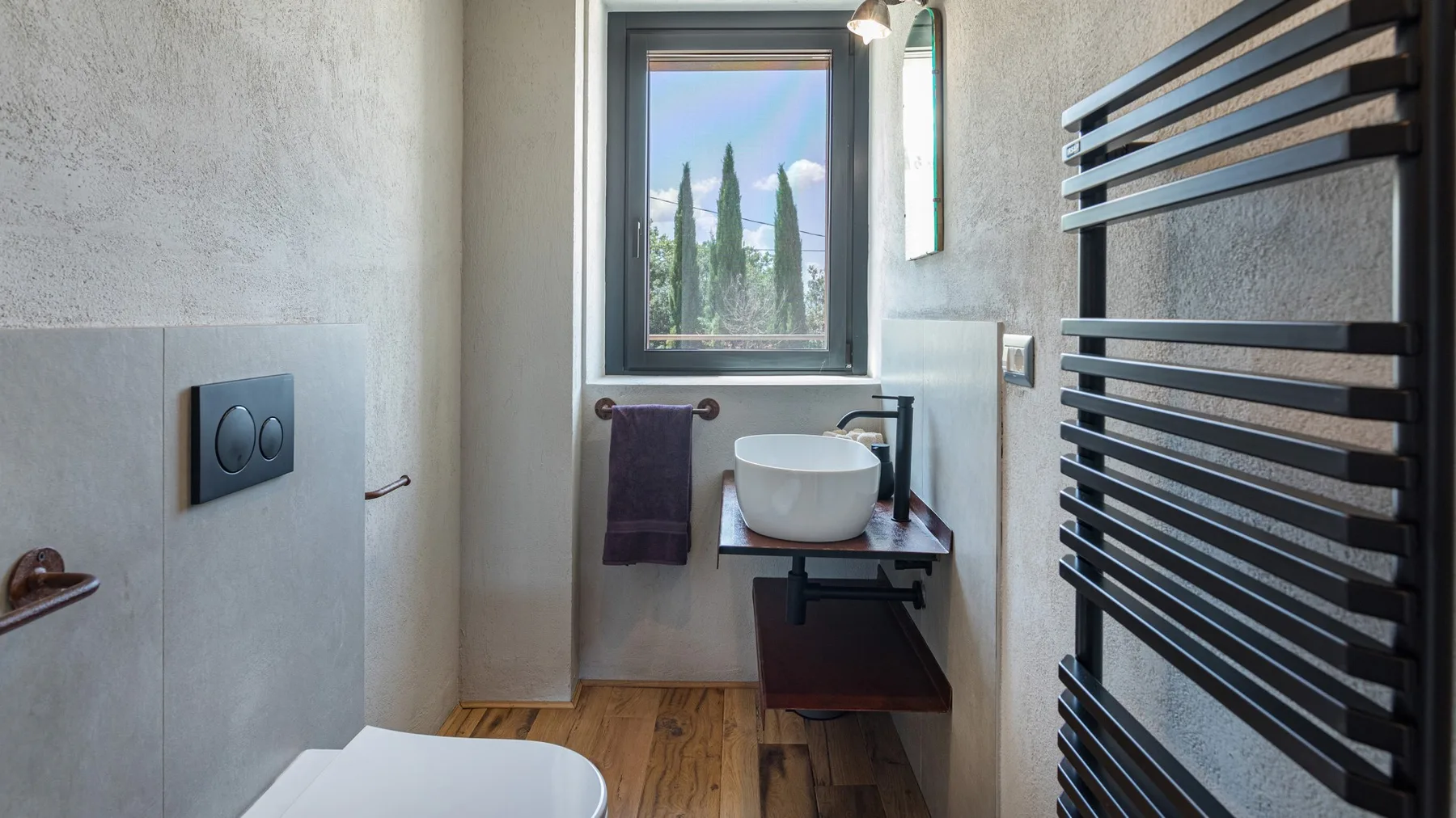 A modern bathroom has a vessel sink on a wall-mounted counter, a towel, and a large black heated towel rail.