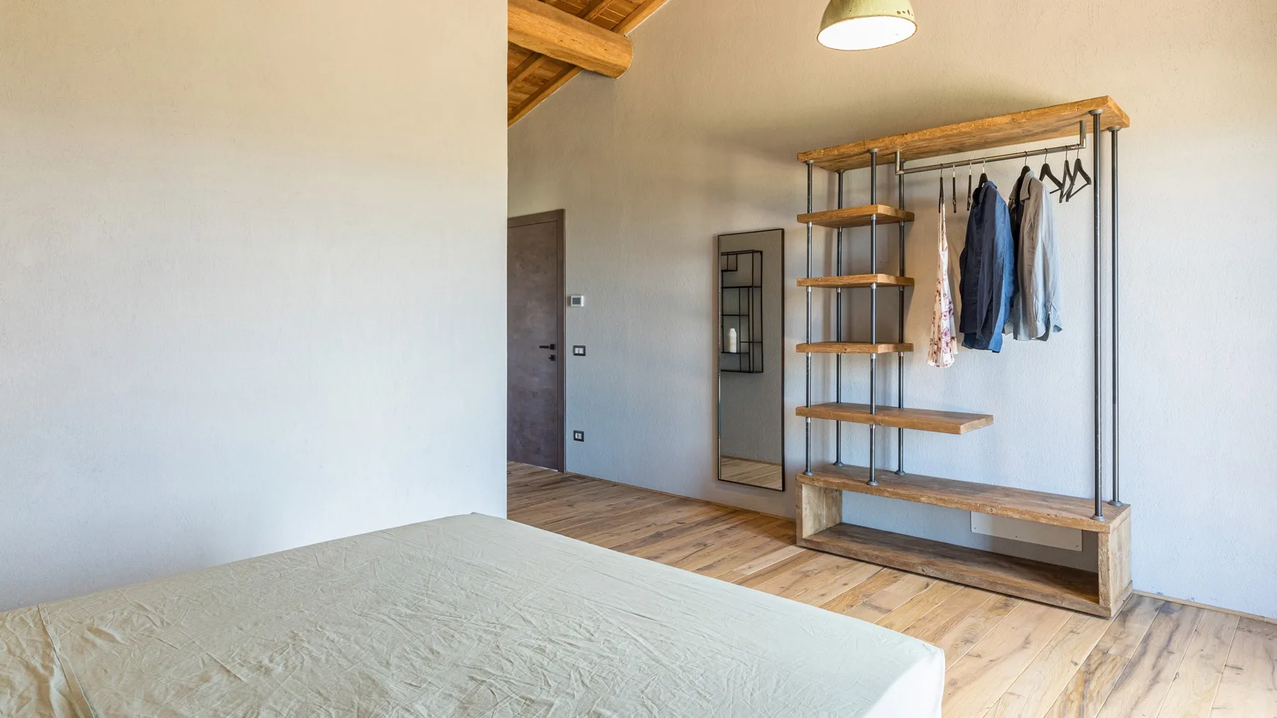 Bedroom with a low bed, exposed wooden ceiling beams, and an open shelving and clothes rail.