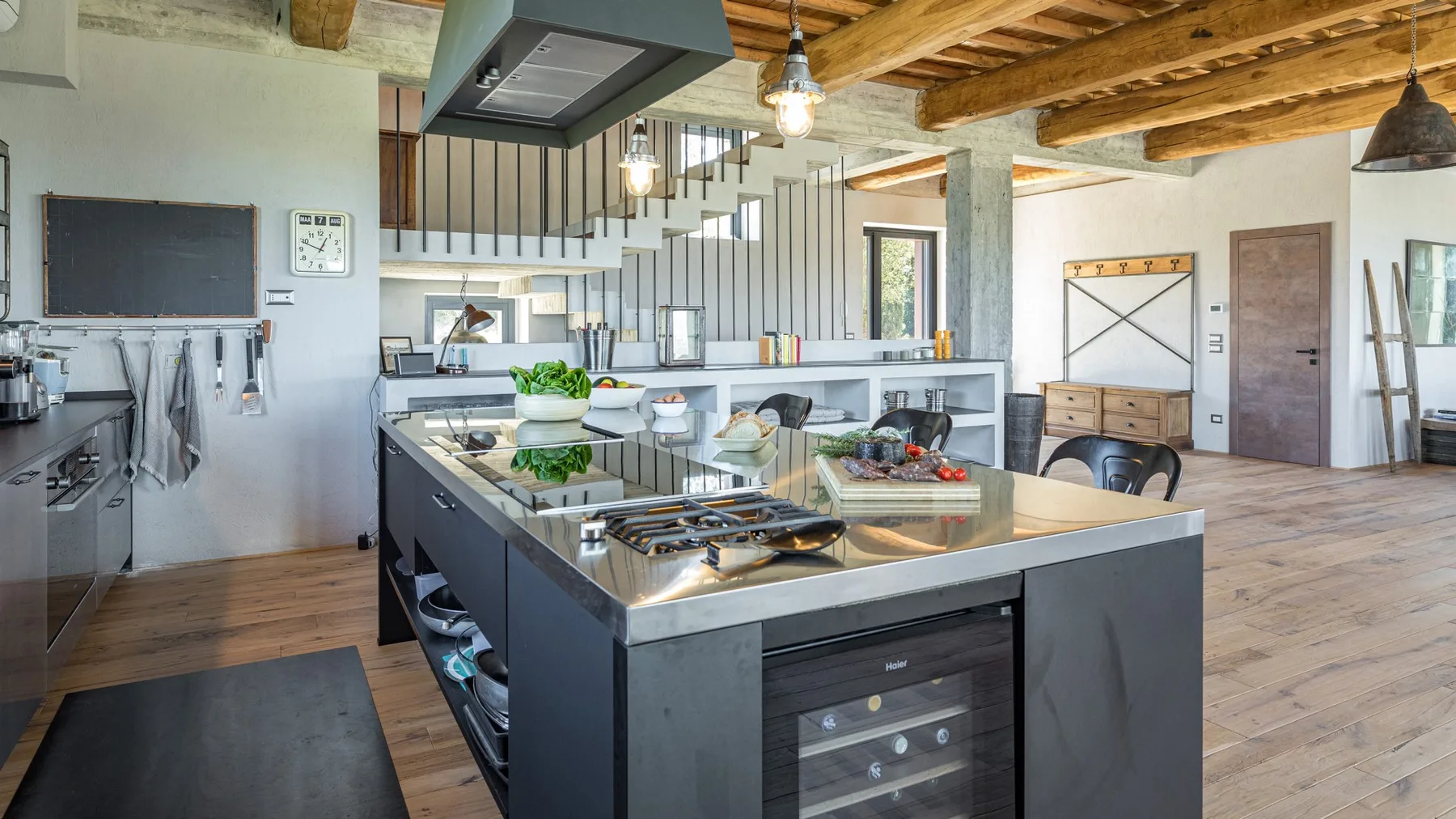 A spacious open-plan kitchen has a large island, stainless steel appliances, and exposed wooden ceiling beams.
