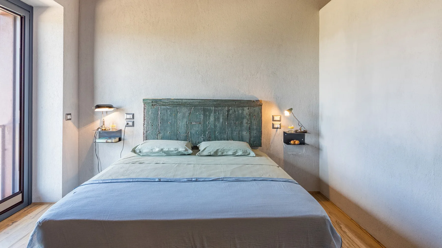 Bedroom with a double bed, a weathered teal headboard, and small wall-mounted bedside shelves.