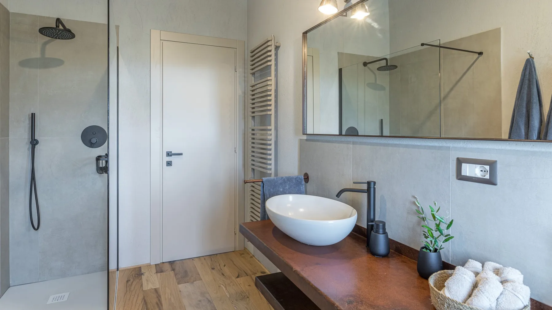 A modern bathroom with a glass shower, wood vanity, white vessel sink, and wall-mounted mirror.