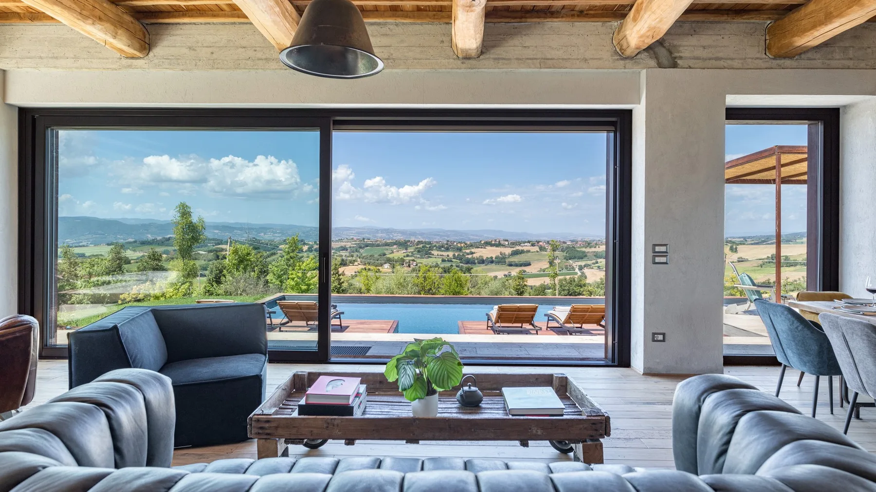 A bright living room opens onto a terrace, with large windows, sofas, and a low wooden coffee table.