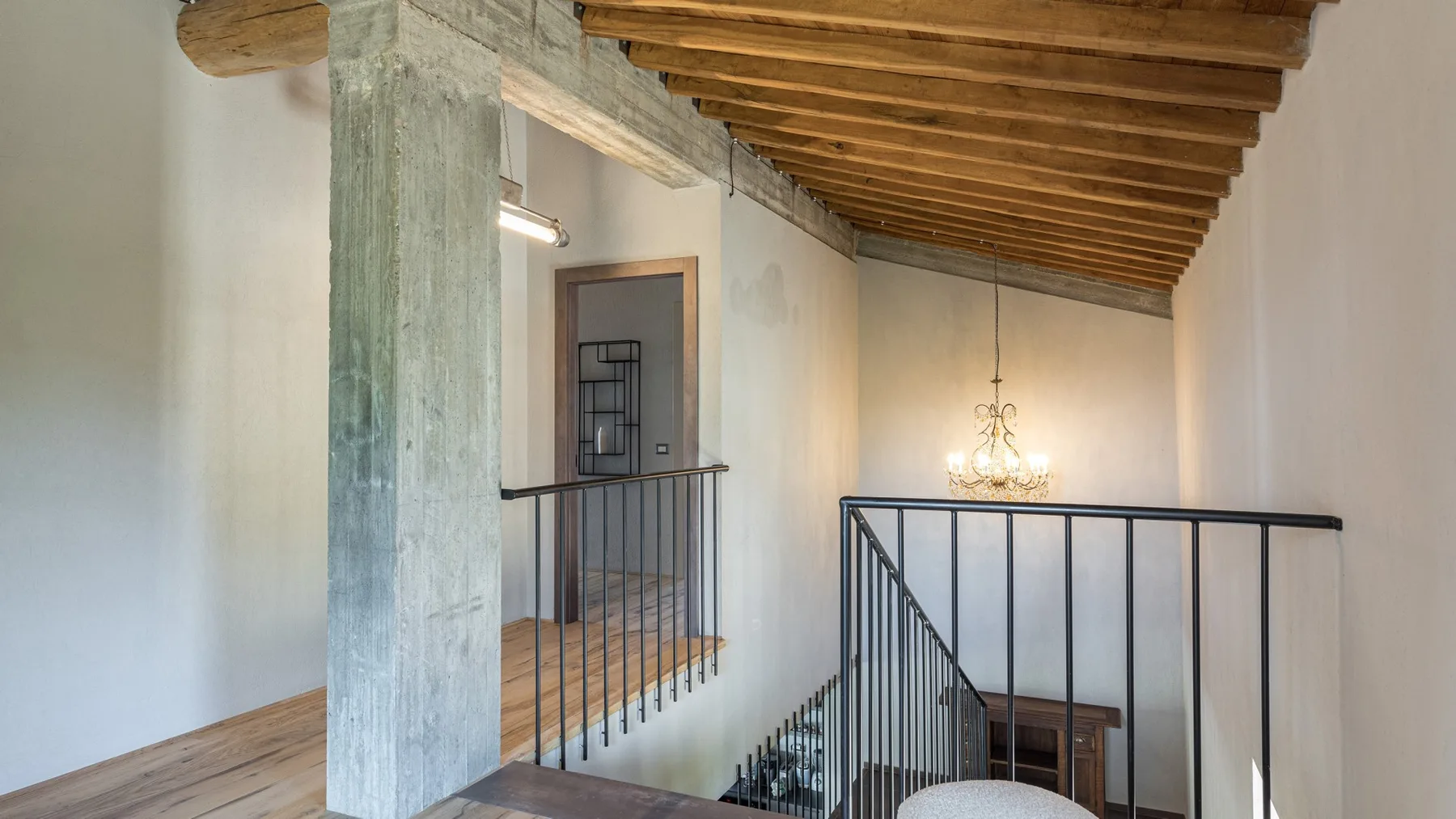 A loft landing with black metal railings, a wooden ceiling, and a chandelier above the stairwell.