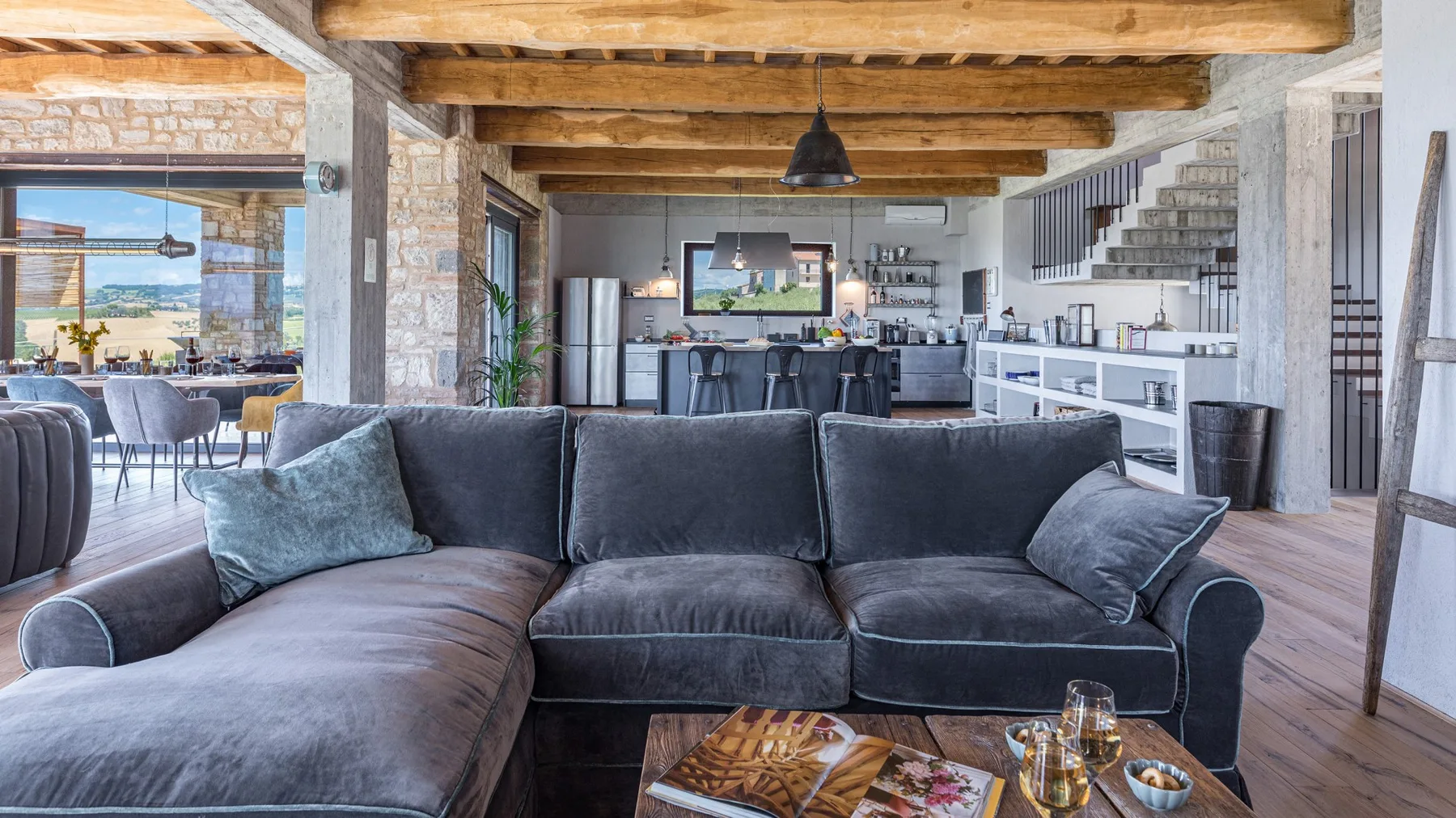 An open-plan living room features a charcoal sectional, exposed timber beams, and a kitchen with a breakfast bar.