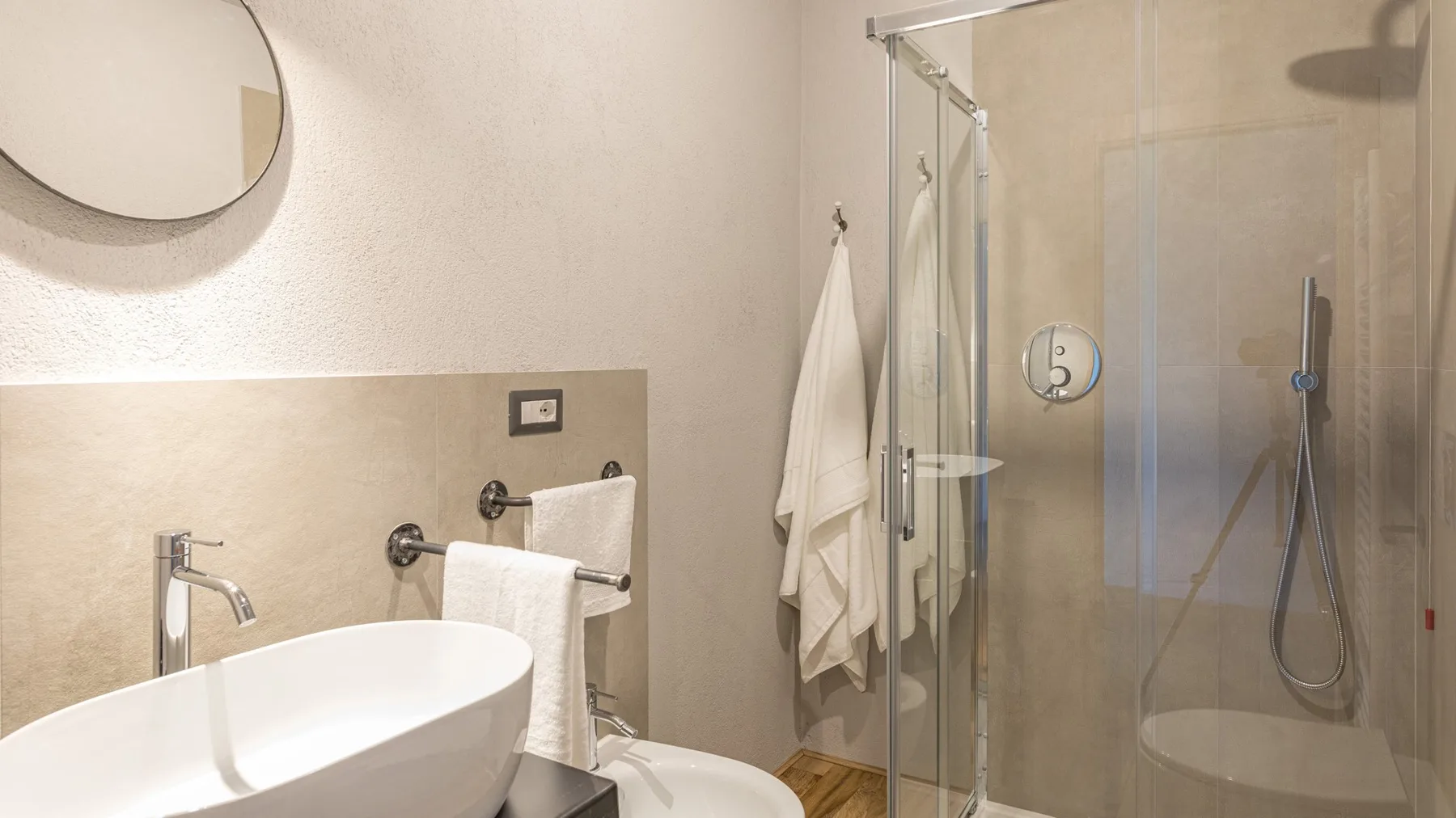 A bright bathroom features a white vessel sink, wall mirror, towel rack, and glass-enclosed shower.