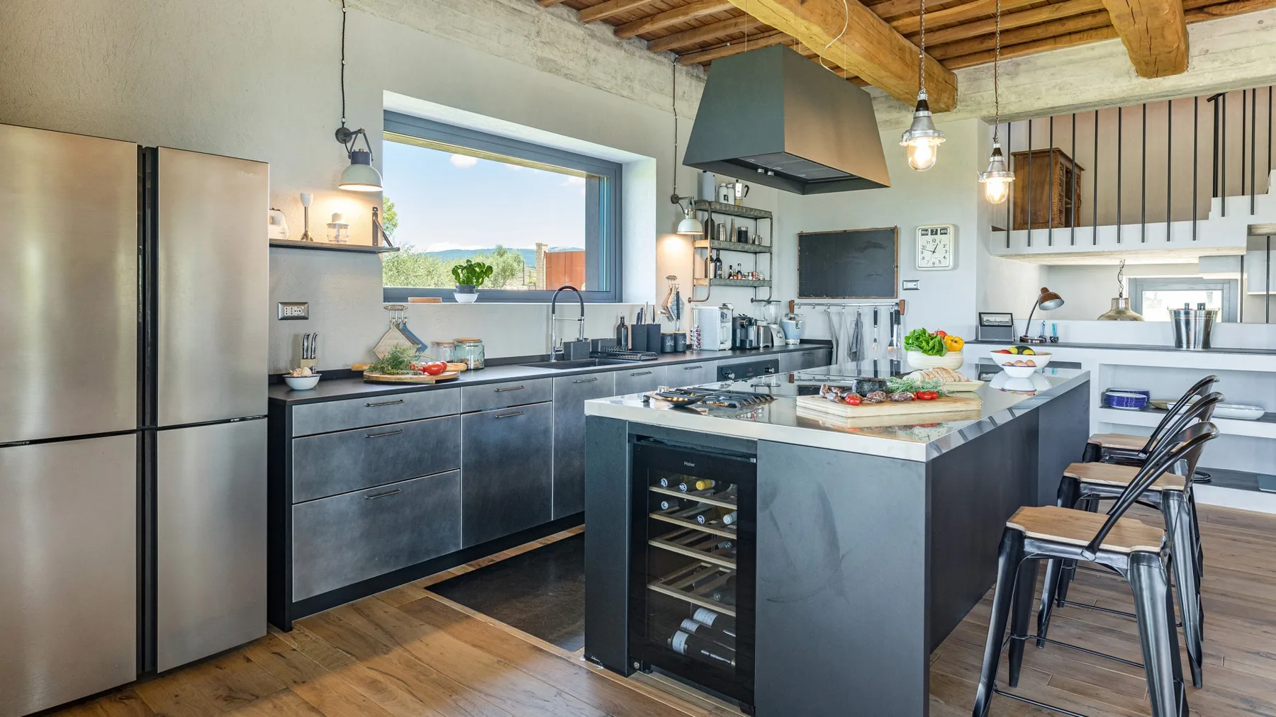 A modern kitchen features dark cabinets, a central island, stainless steel appliances, and a wood-beam ceiling.