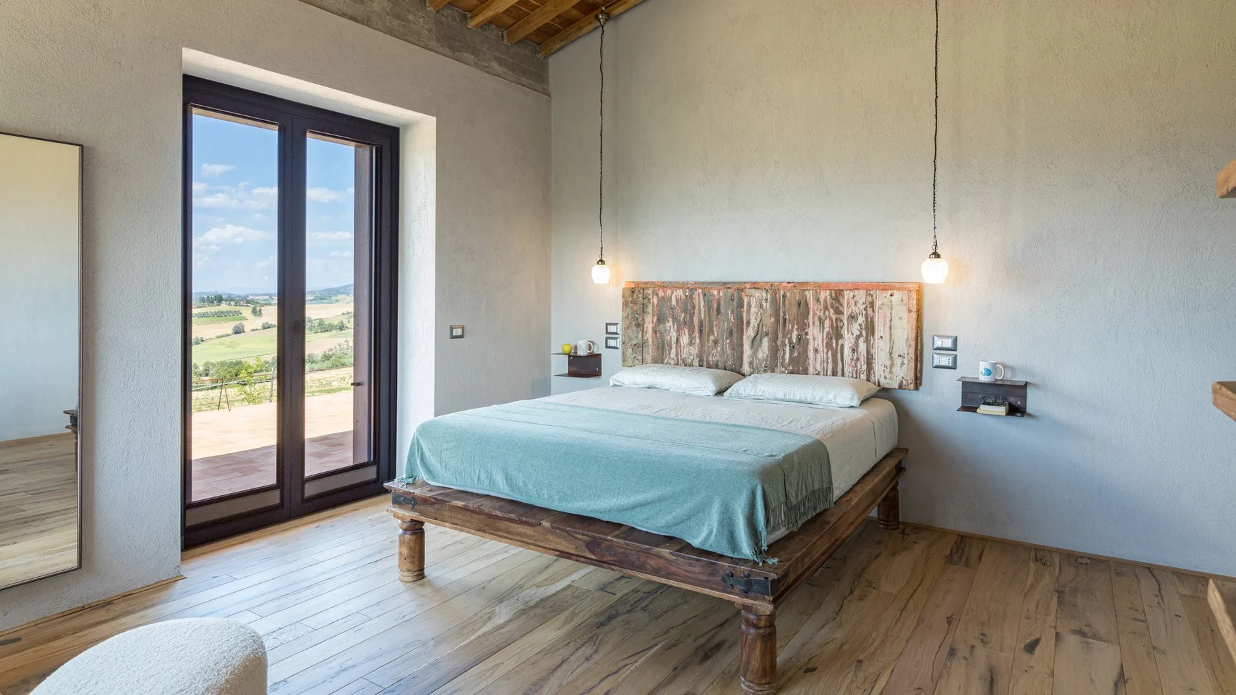 A bedroom with a wooden bed, pale blue bedding, and glass doors opening onto a balcony.