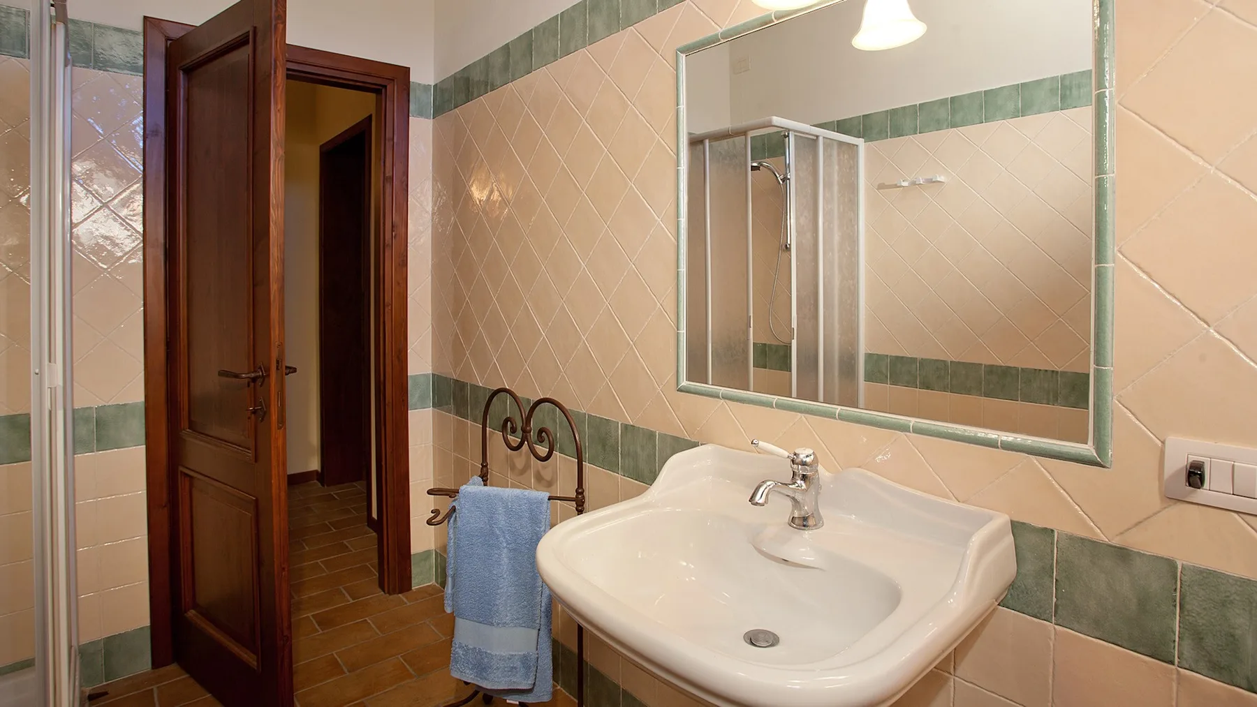 A tiled bathroom with a sink, mirror, and open wooden door.
