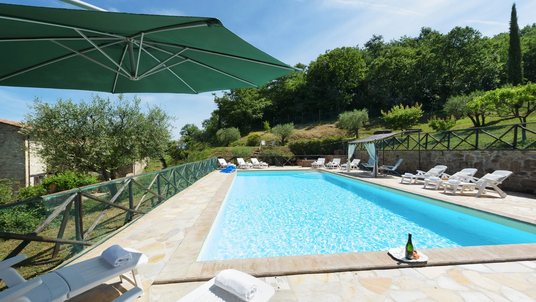 An outdoor swimming pool is surrounded by loungers and greenery.