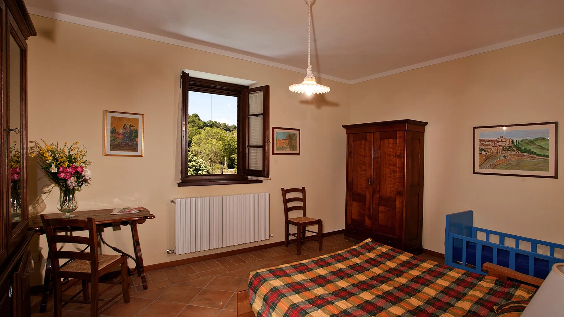 A bedroom with a plaid bedspread, wooden wardrobe, and an open window.