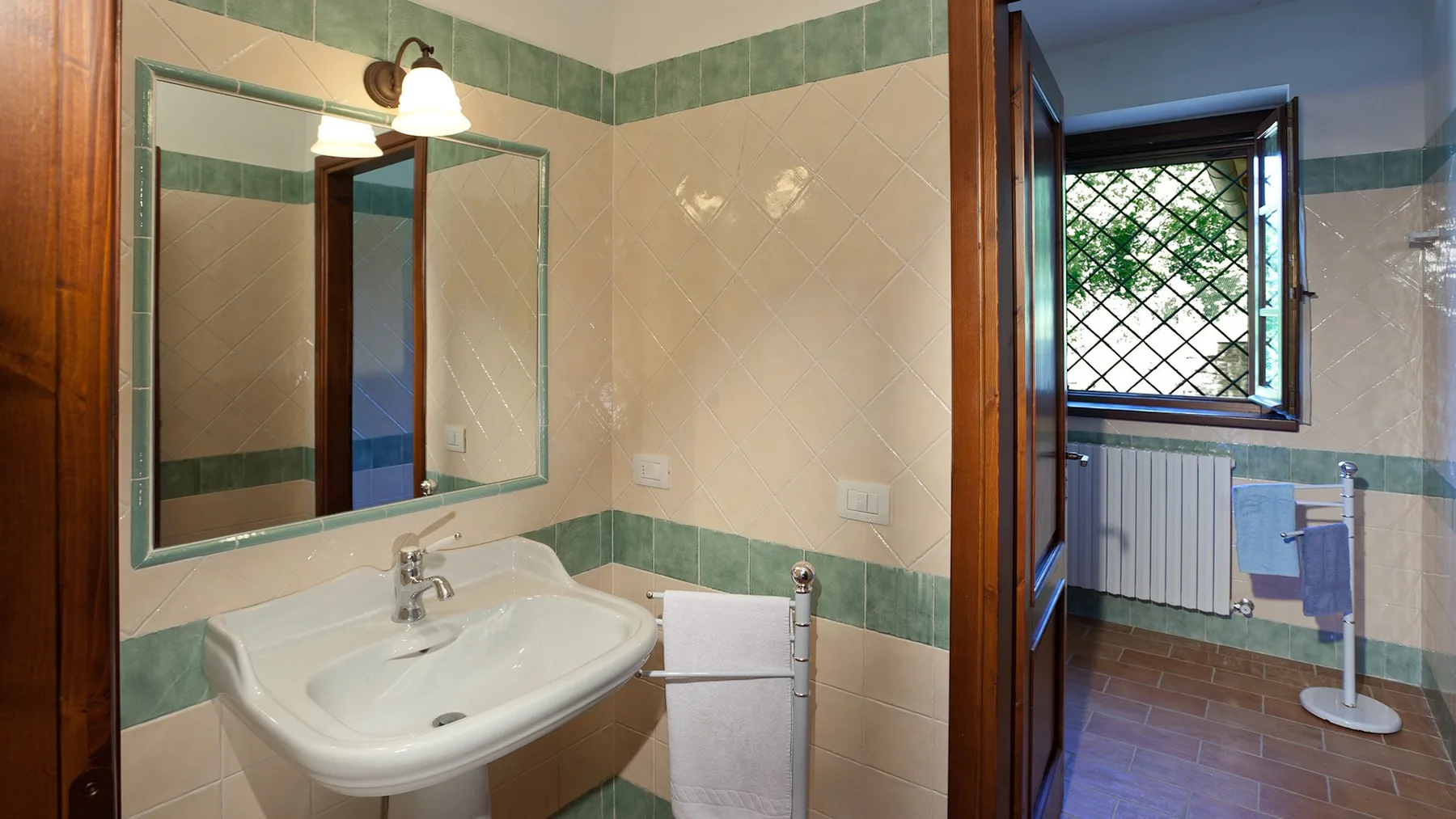 A tiled bathroom with a wall mirror, sink, and doorway to a windowed room.