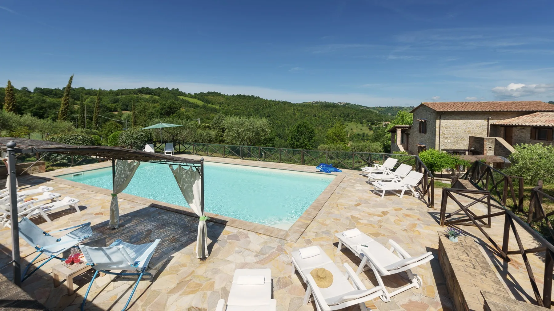 An outdoor swimming pool sits beside a paved terrace with lounge chairs.