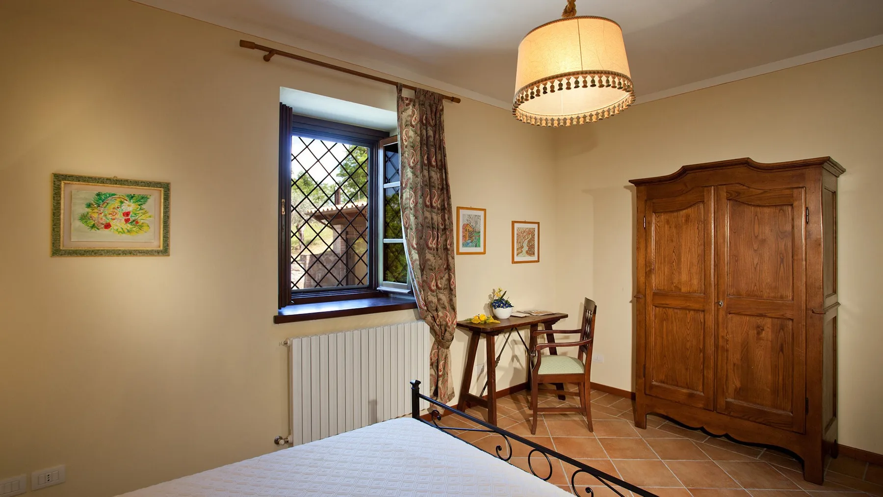 A bedroom with a bed, a wooden wardrobe, and a window with patterned curtains.
