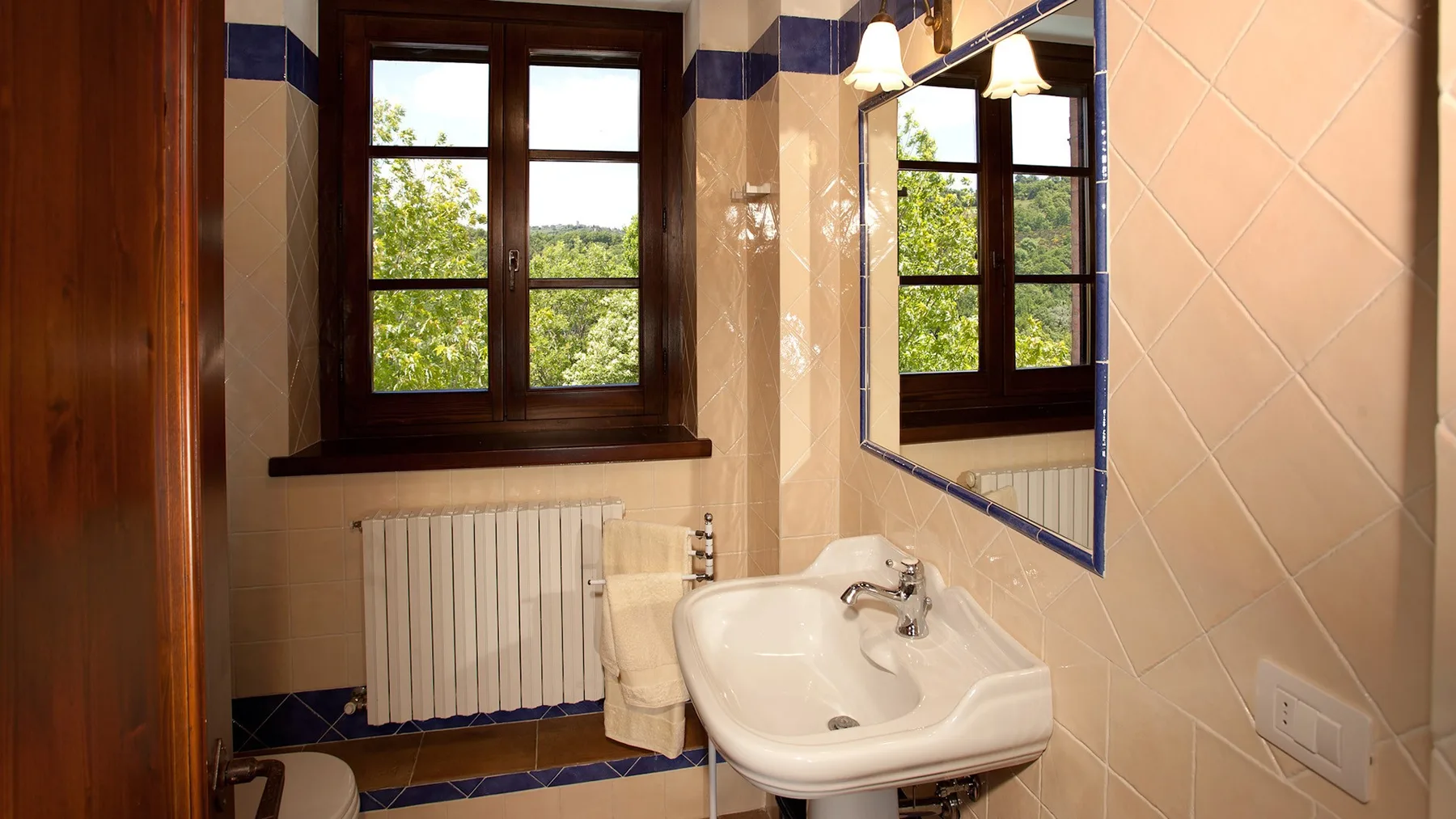 A bathroom with a white sink, radiator, and windows overlooking greenery.