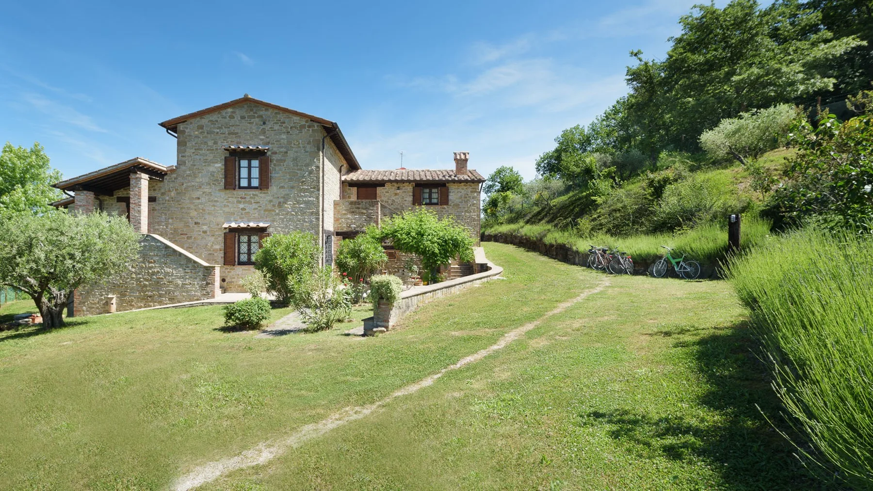 A stone house stands beside a broad lawn and leafy trees.