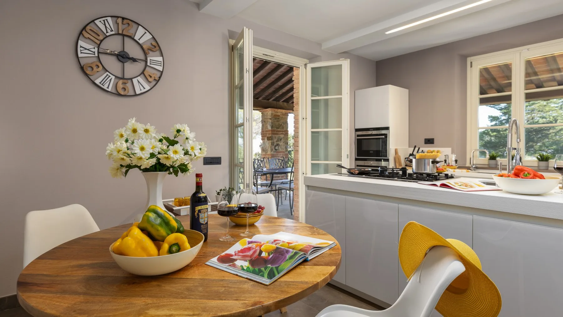 A dining area with a round wooden table, fruit, and flowers beside the kitchen.