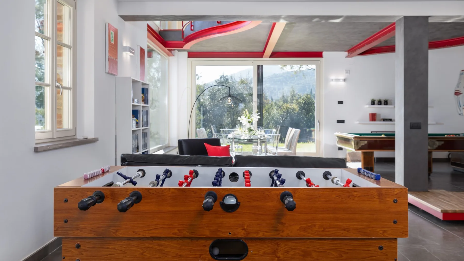 A bright game room with a foosball table and large windows overlooking greenery.