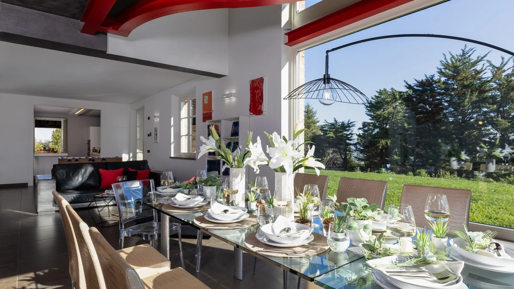 A bright dining area has a glass table set with dishes beside large windows.