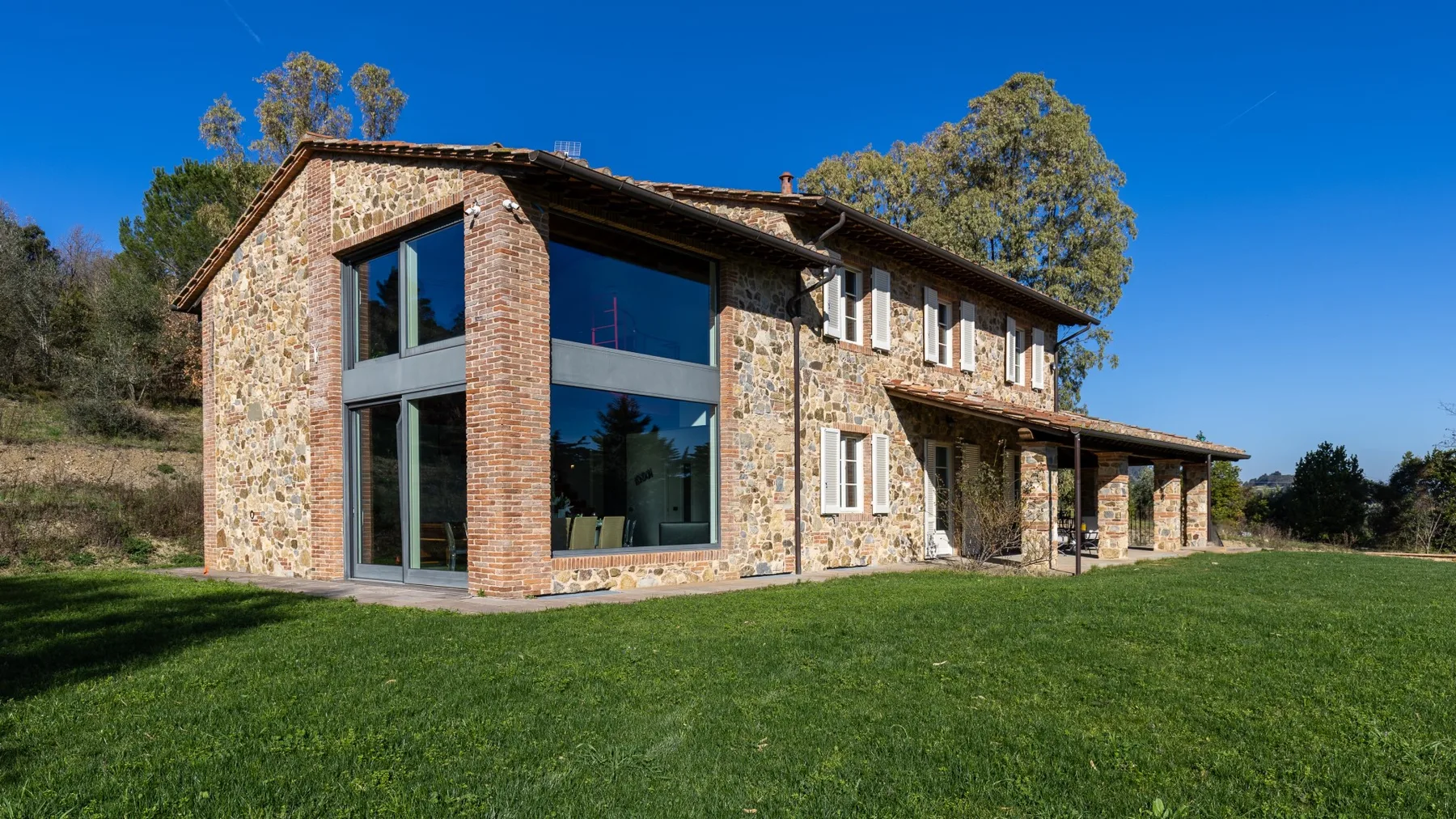 A stone house with large windows stands beside a broad green lawn.