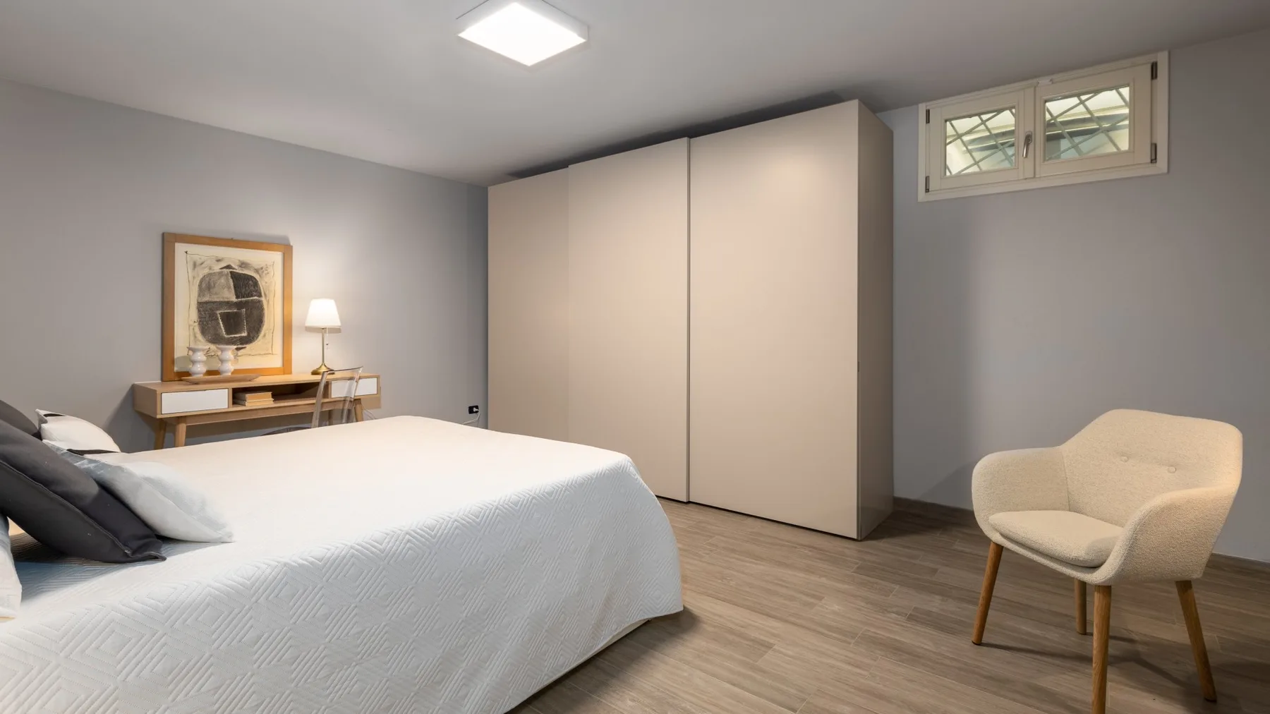 A bedroom with a neatly made bed and an upholstered chair.
