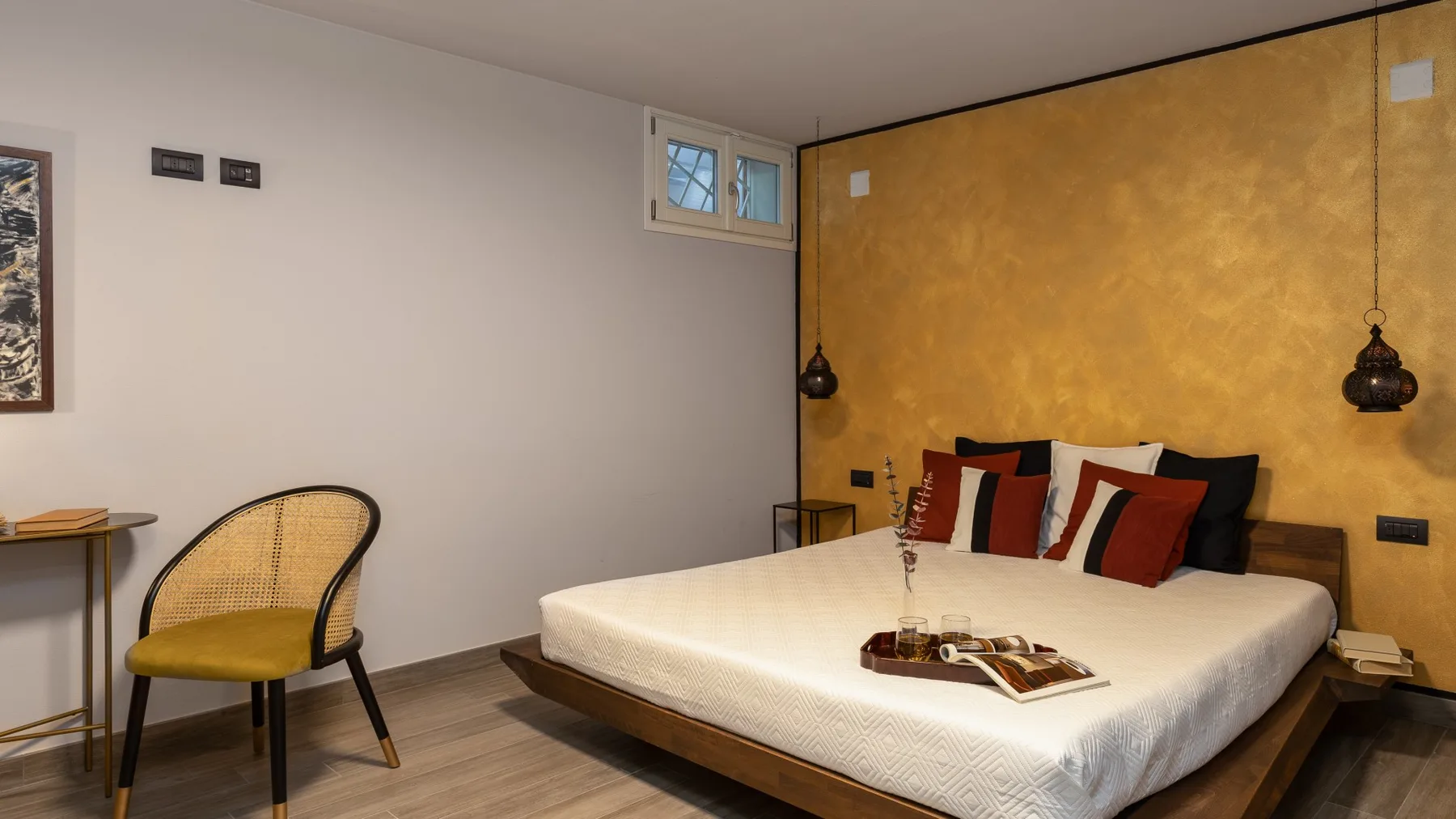 A bedroom with a large bed against a textured ochre wall.