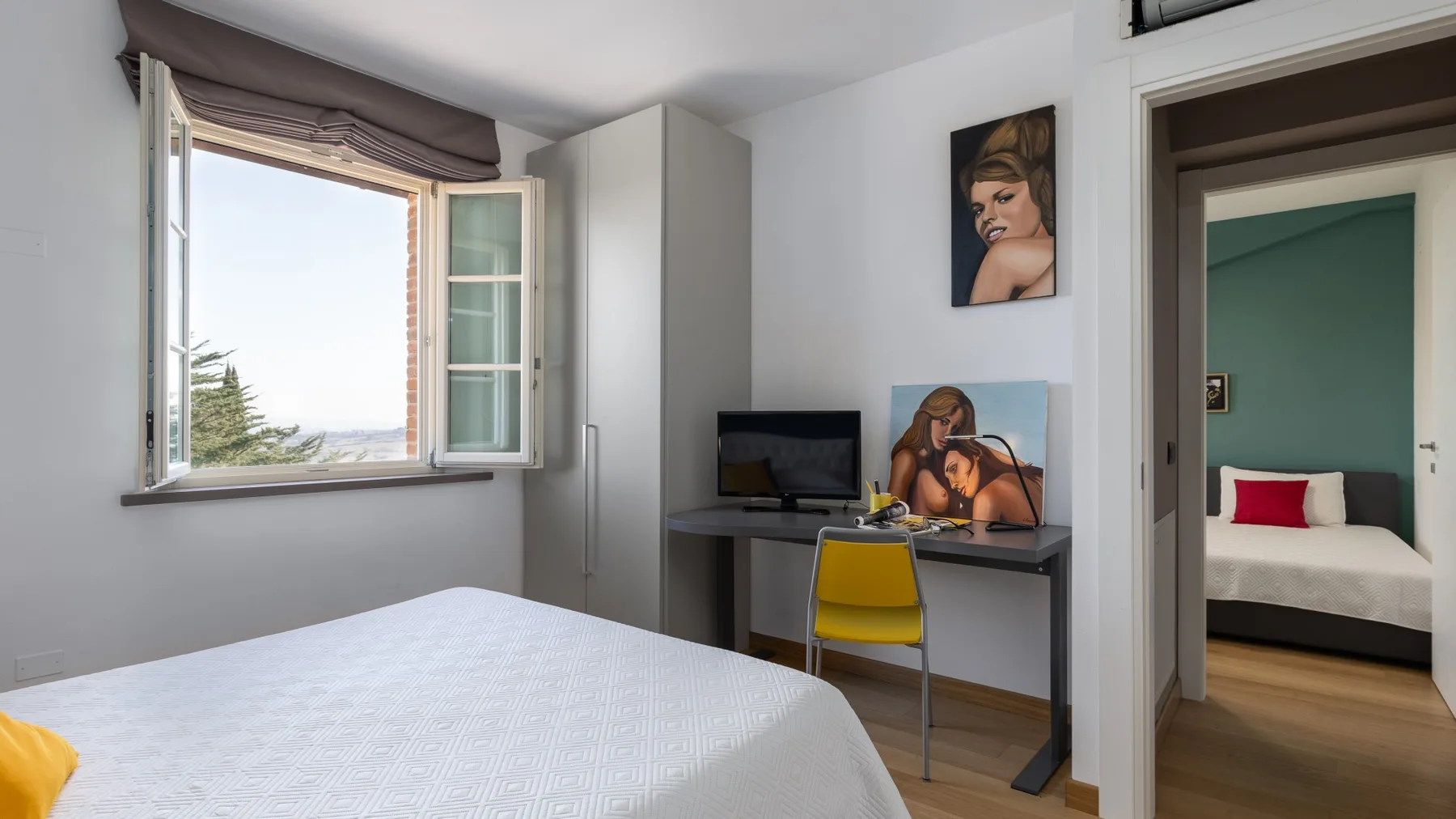 A bright bedroom with a bed beside a desk and an open window.