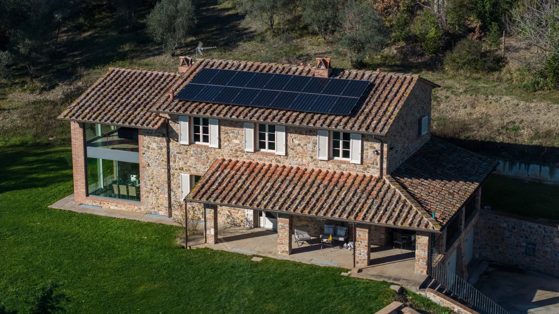 Aerial view of a stone house with tiled roofs and solar panels.