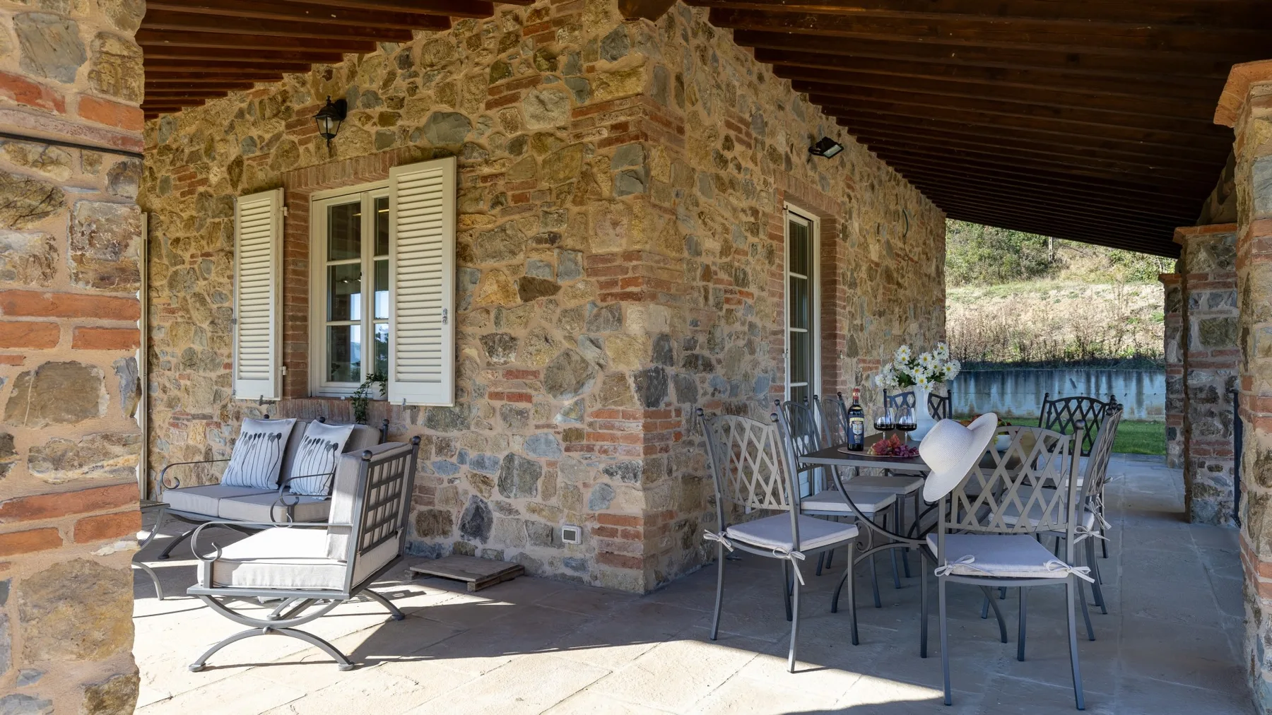A covered stone patio with outdoor seating and a dining table.