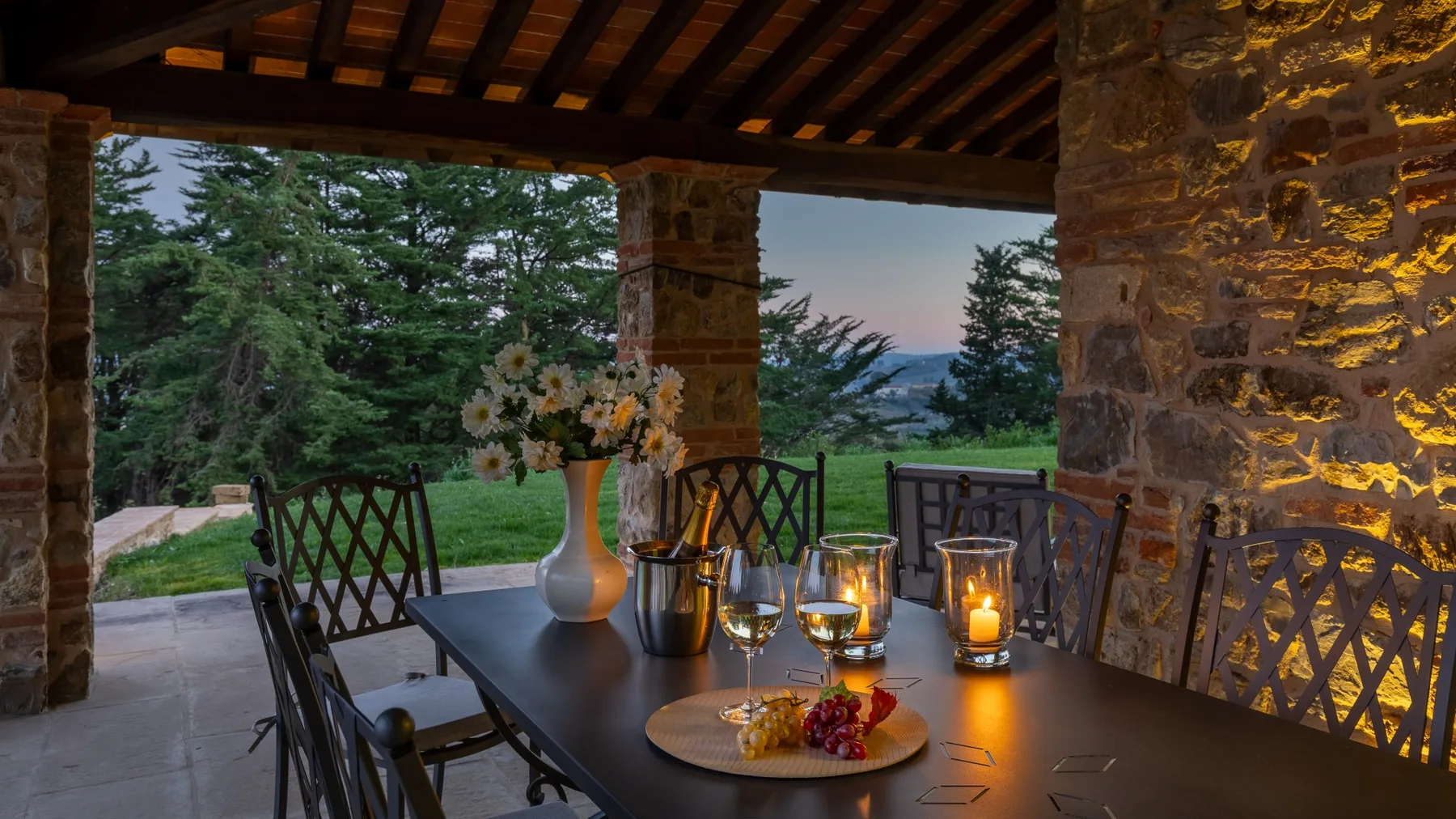 A covered outdoor dining area with a table set beside a garden and trees.