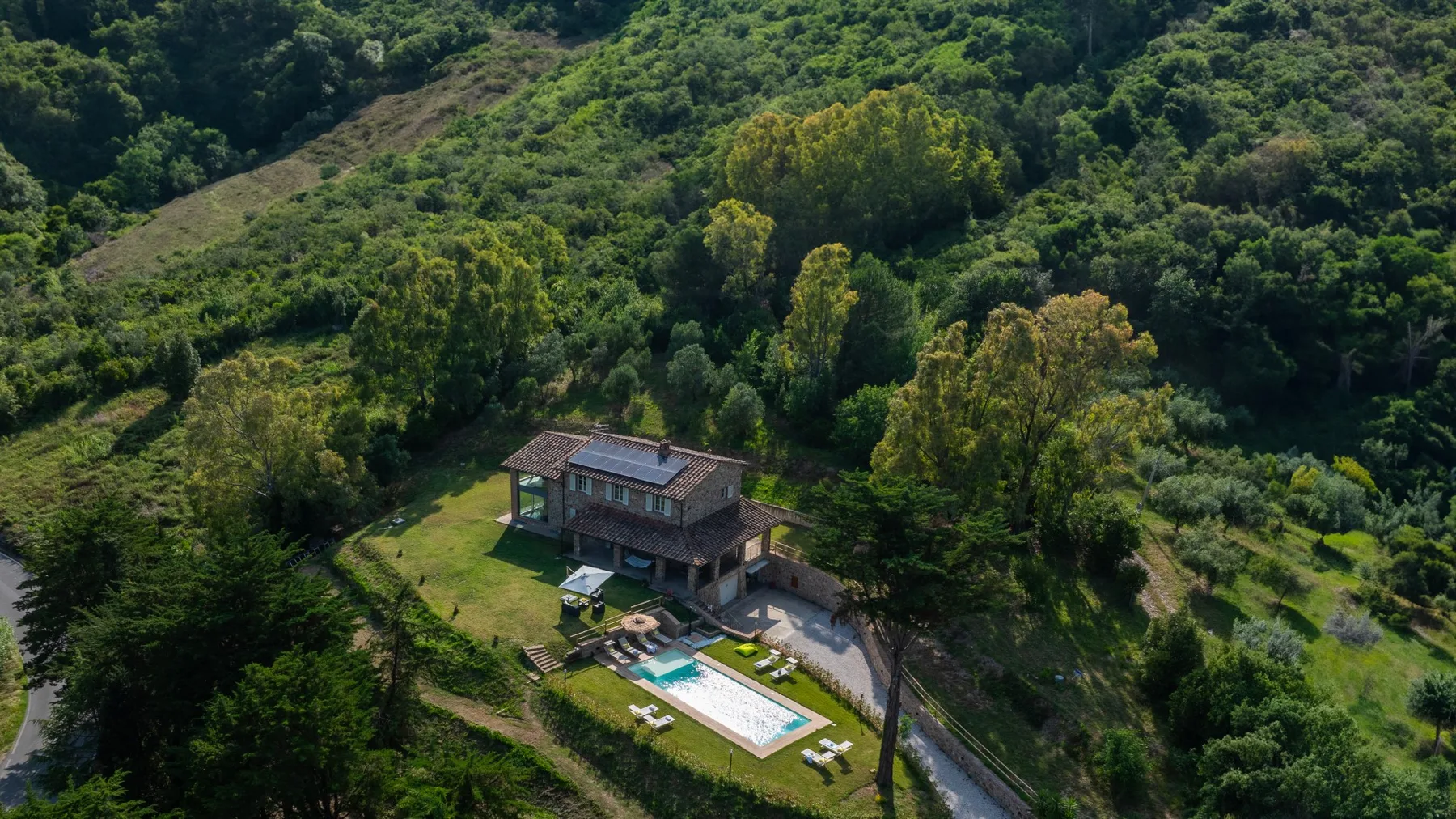 An aerial view of a house and swimming pool amid wooded hills.