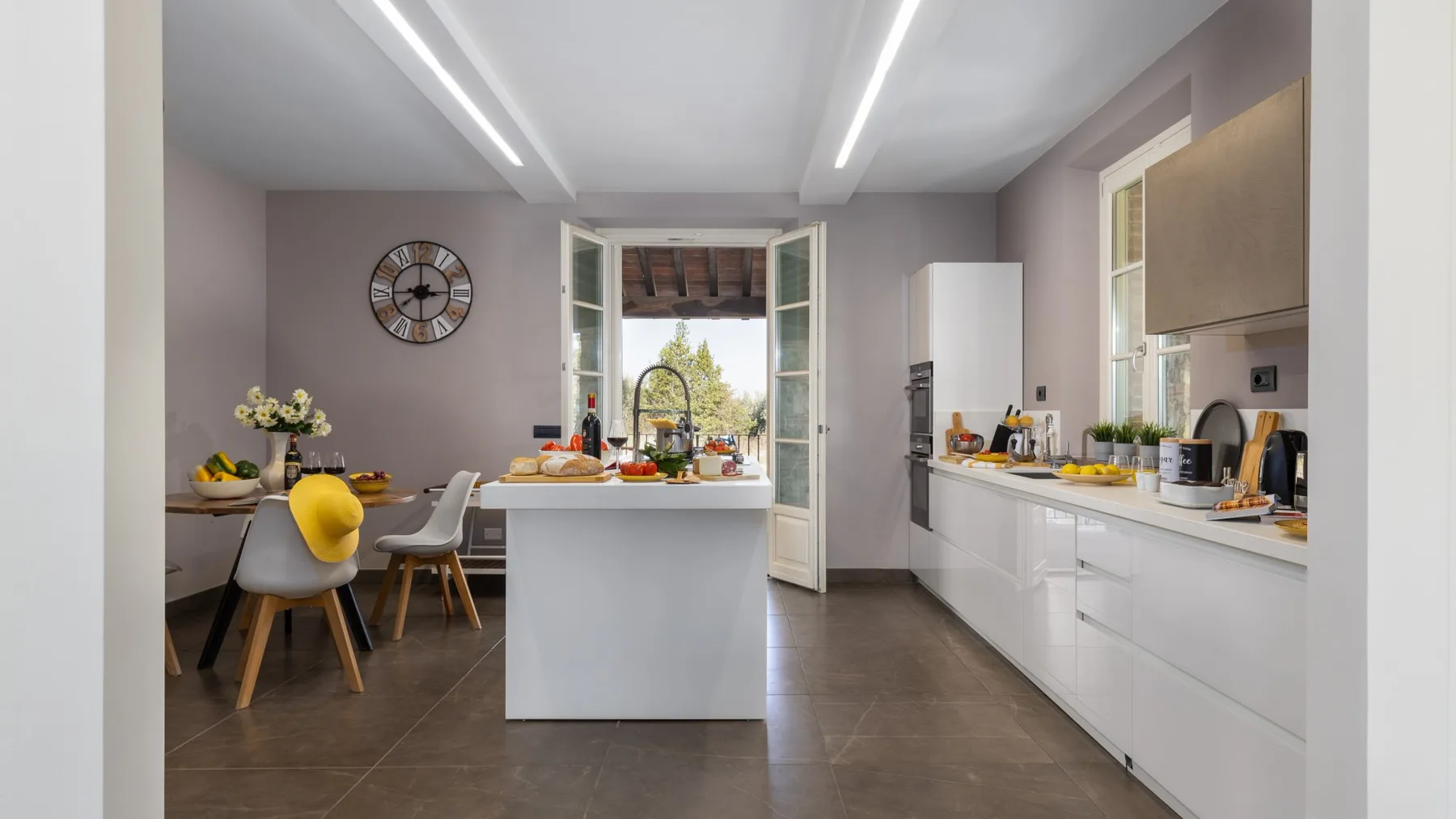 A bright kitchen with a central island, dining table, and open doors to a patio.