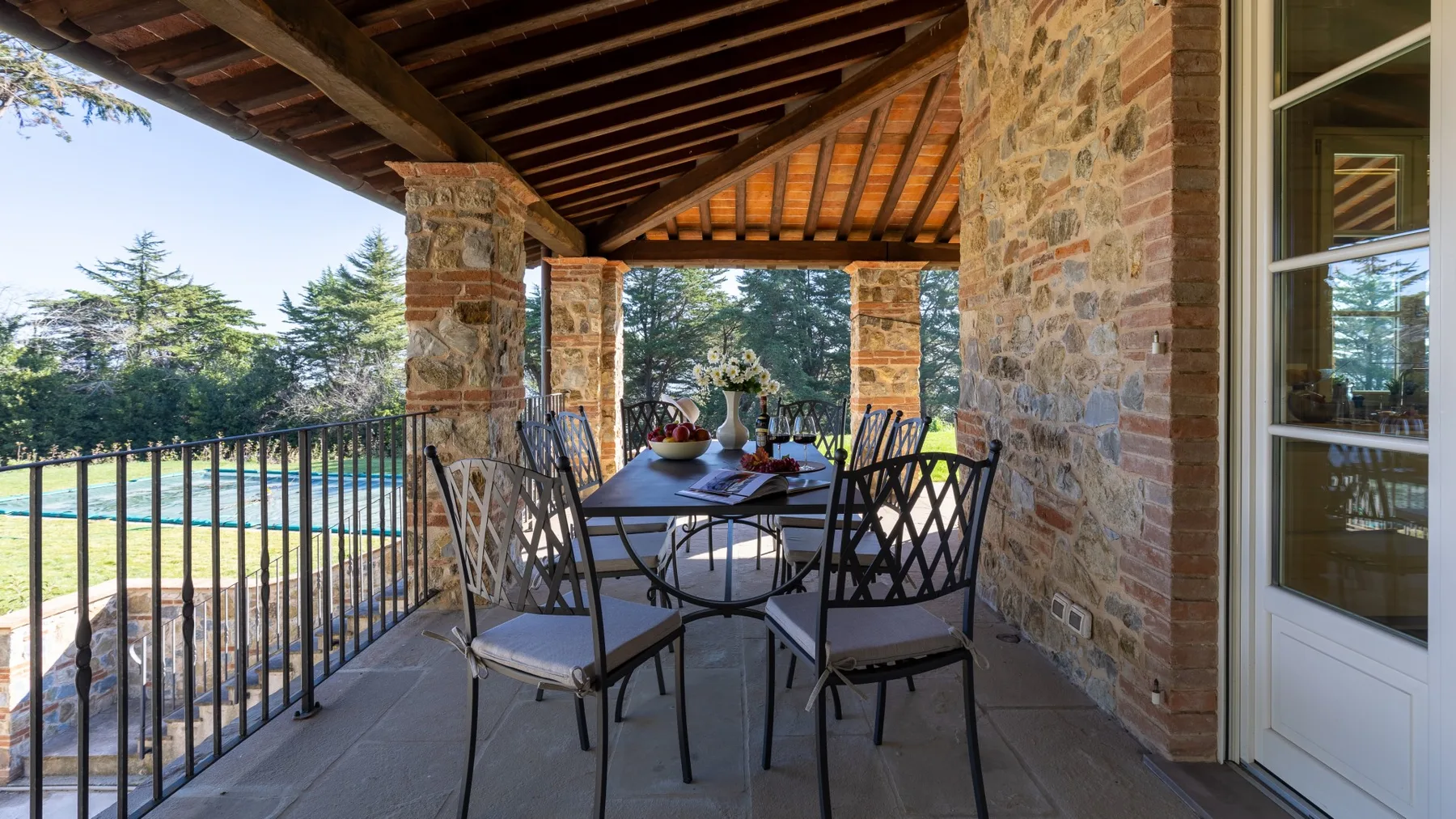 A covered stone terrace with a dining table and chairs overlooks a landscaped outdoor area.