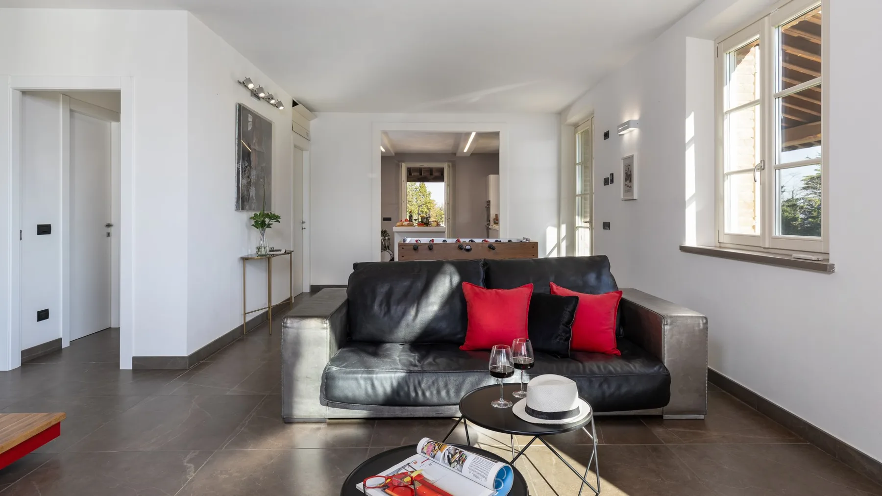 A bright living room with dark seating and red cushions.