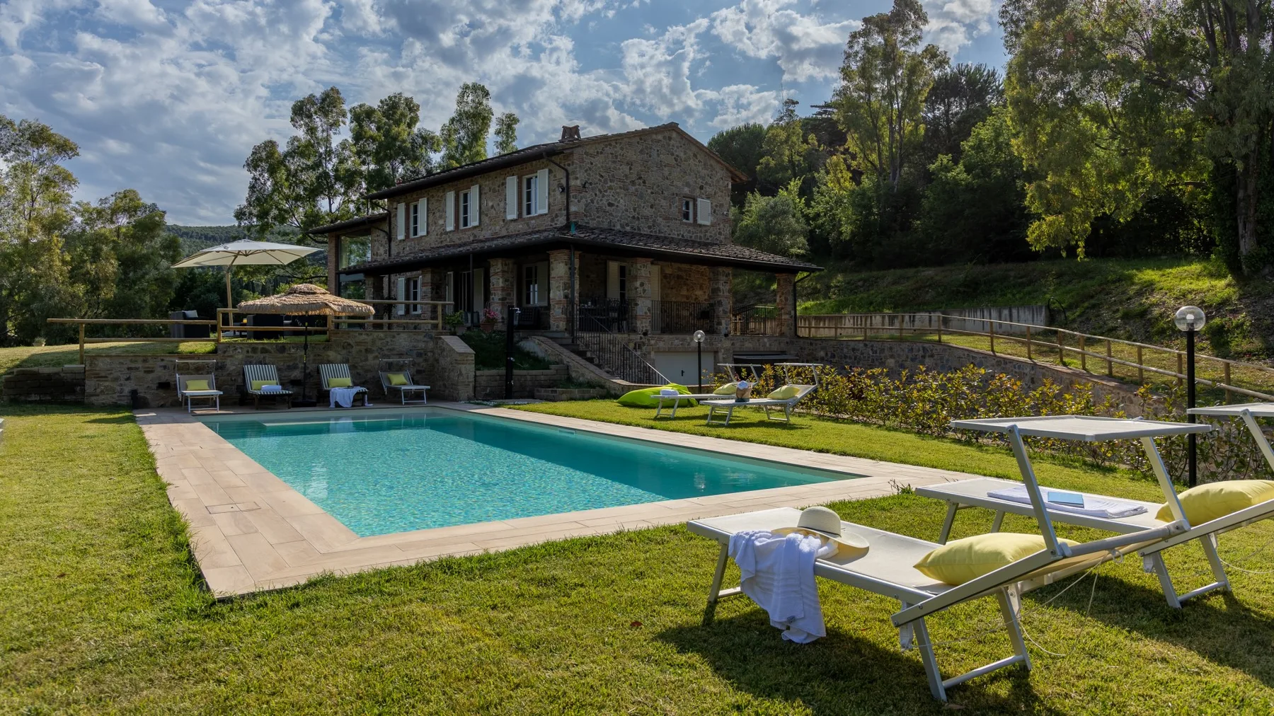 A stone house stands beside an outdoor swimming pool and lawn.