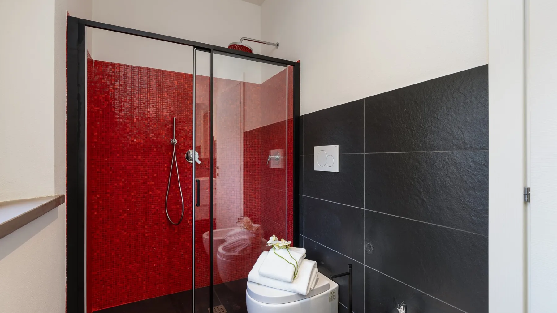 A bathroom shower with red tiled walls and folded towels.