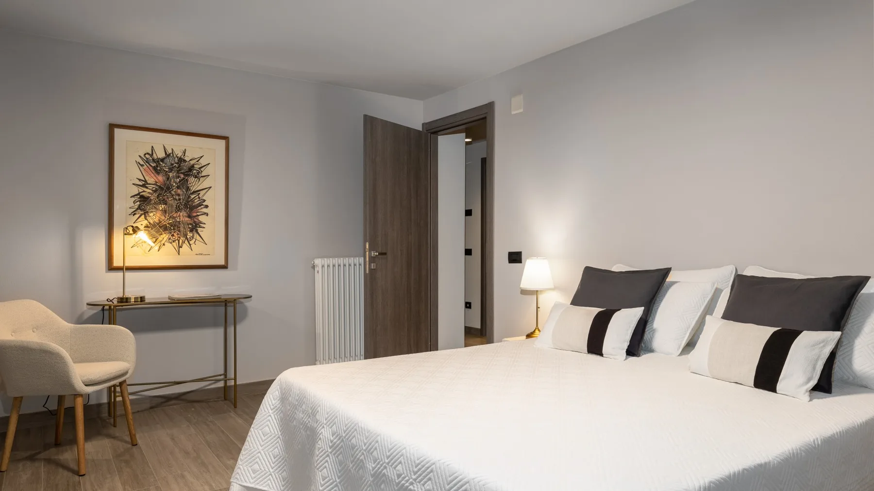 A bedroom with a neatly made bed, bedside lamp, and framed wall art.