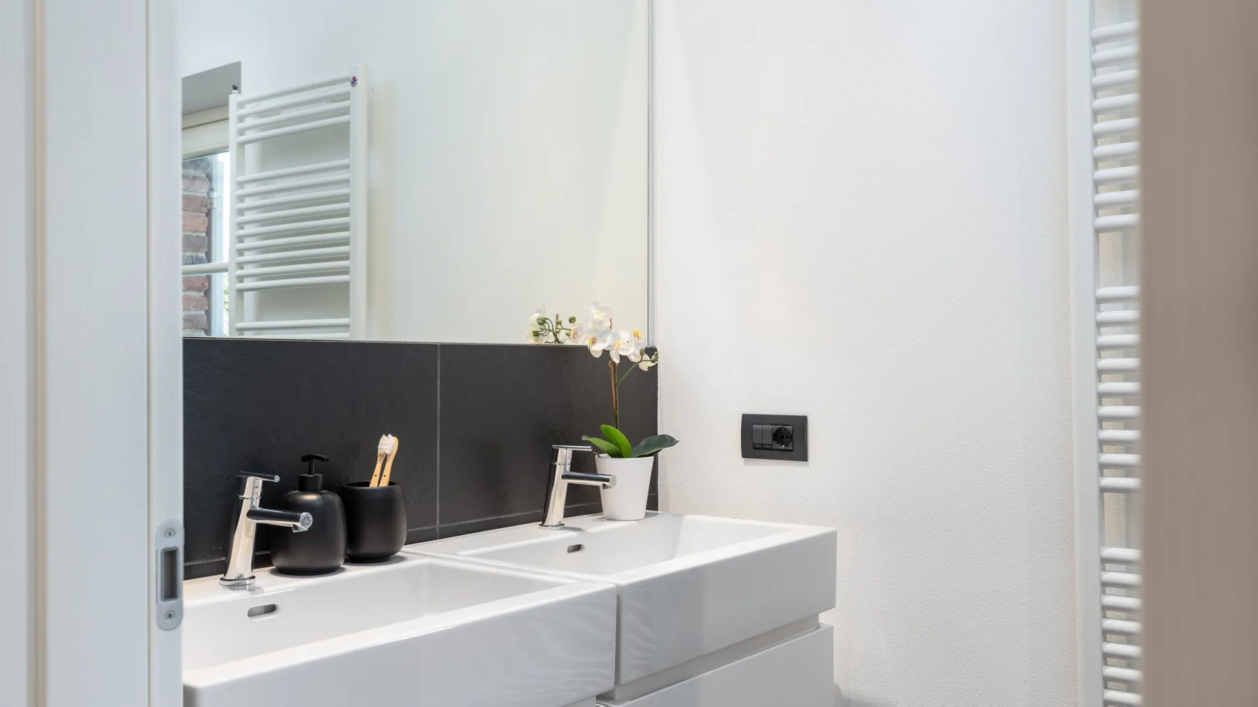 A bathroom vanity with a white sink, dark backsplash, and wall-mounted faucet.
