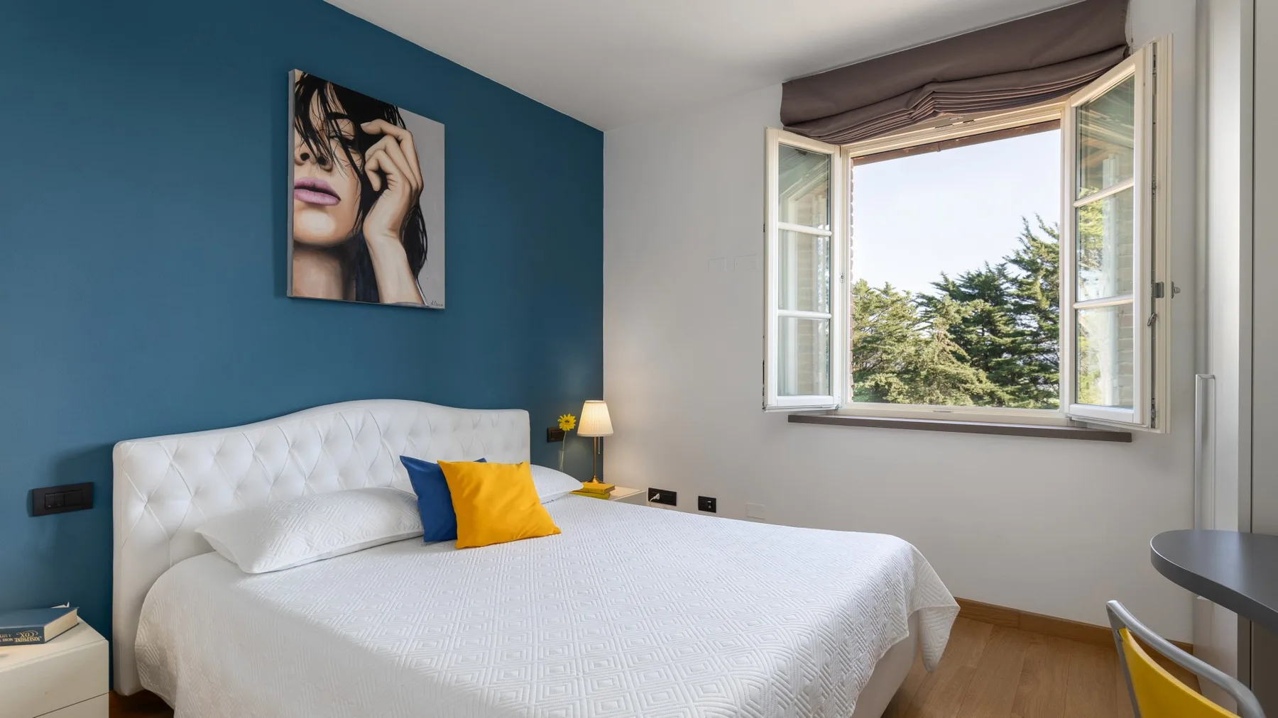 A bedroom with a white bed, colorful cushions, and an open window.