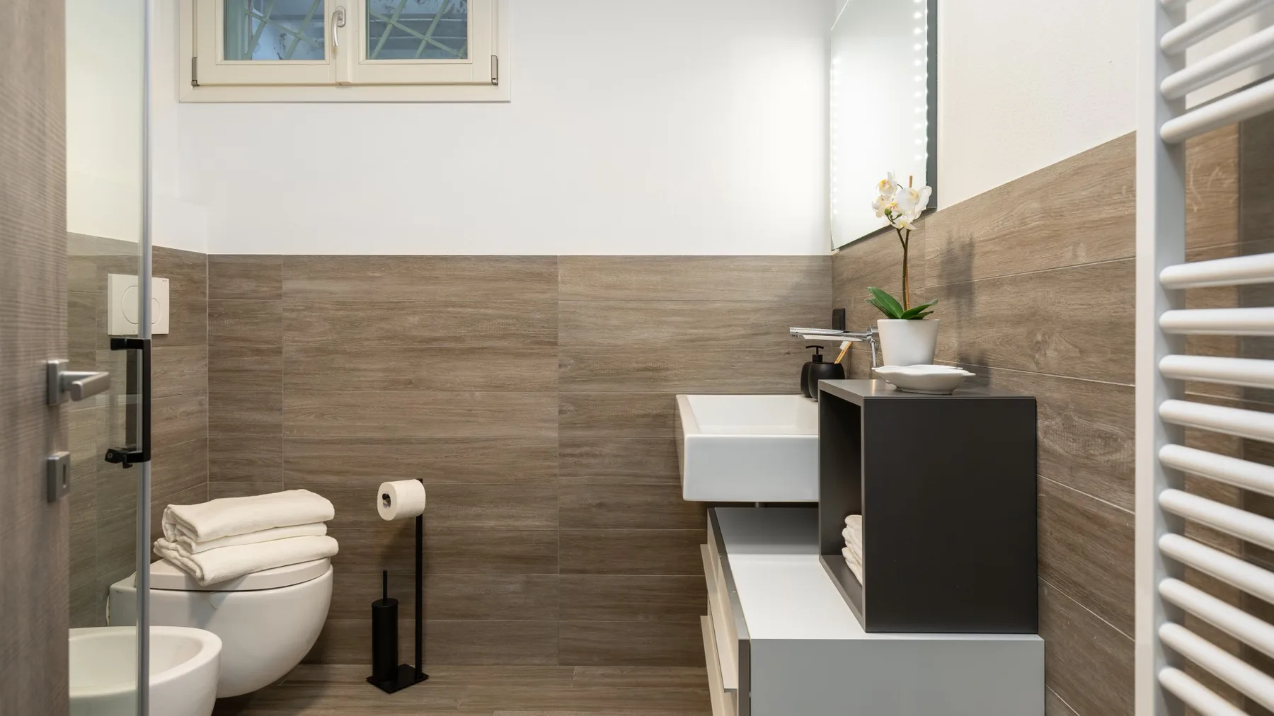 A bathroom with a sink, toilet, and shower area behind a glass panel.