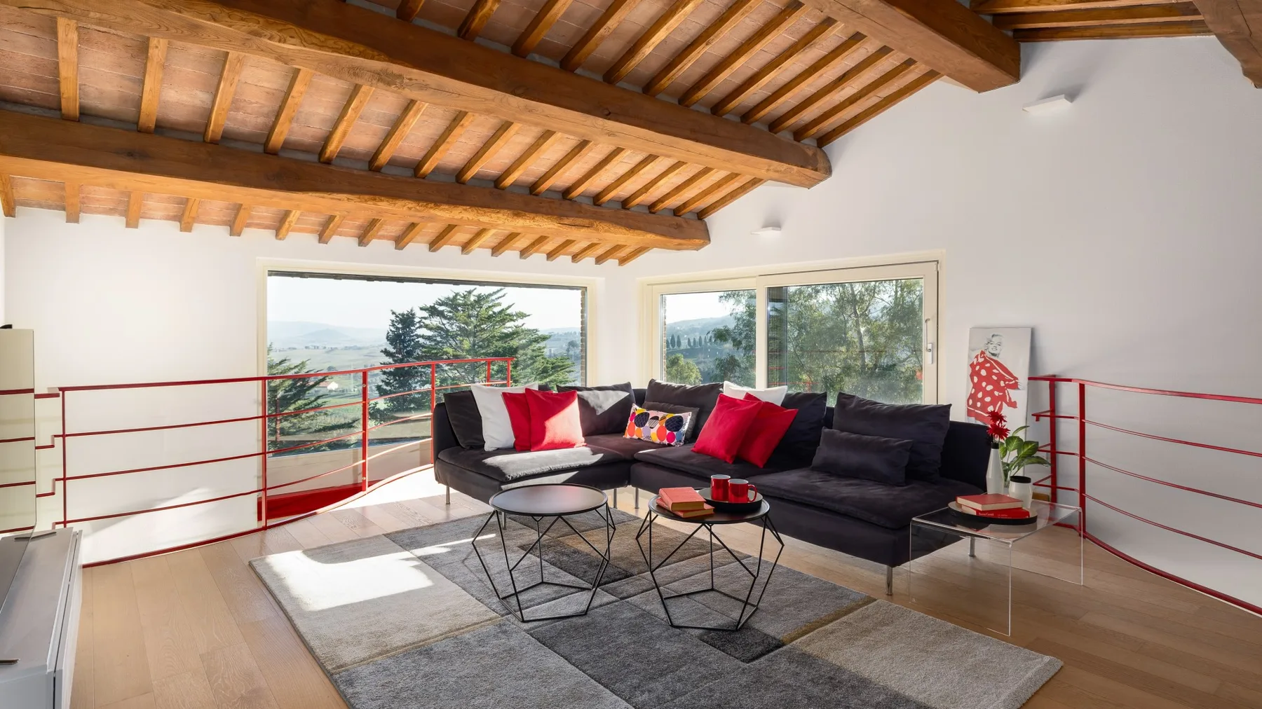 A living room with dark seating, red accents, and large windows.